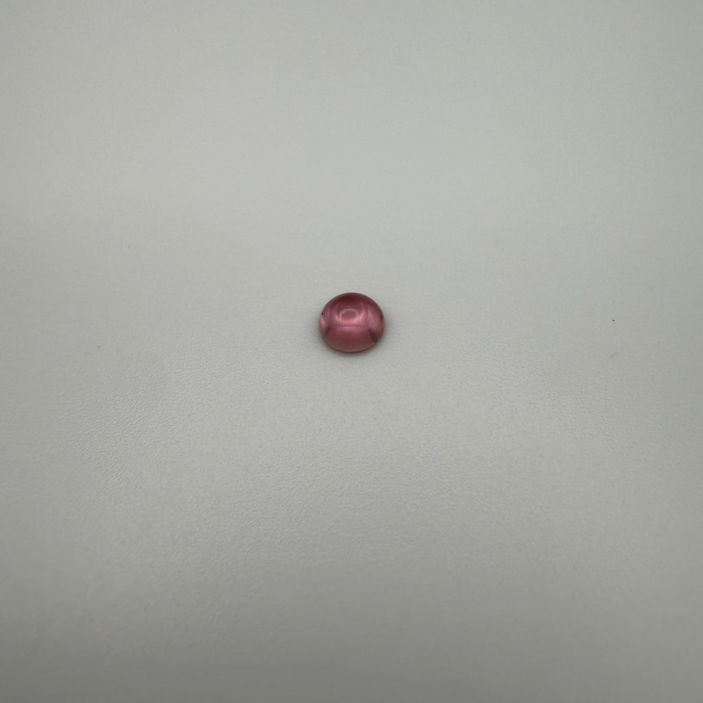 macro view of a pink tourmaline round cabochon on a smooth white surface
