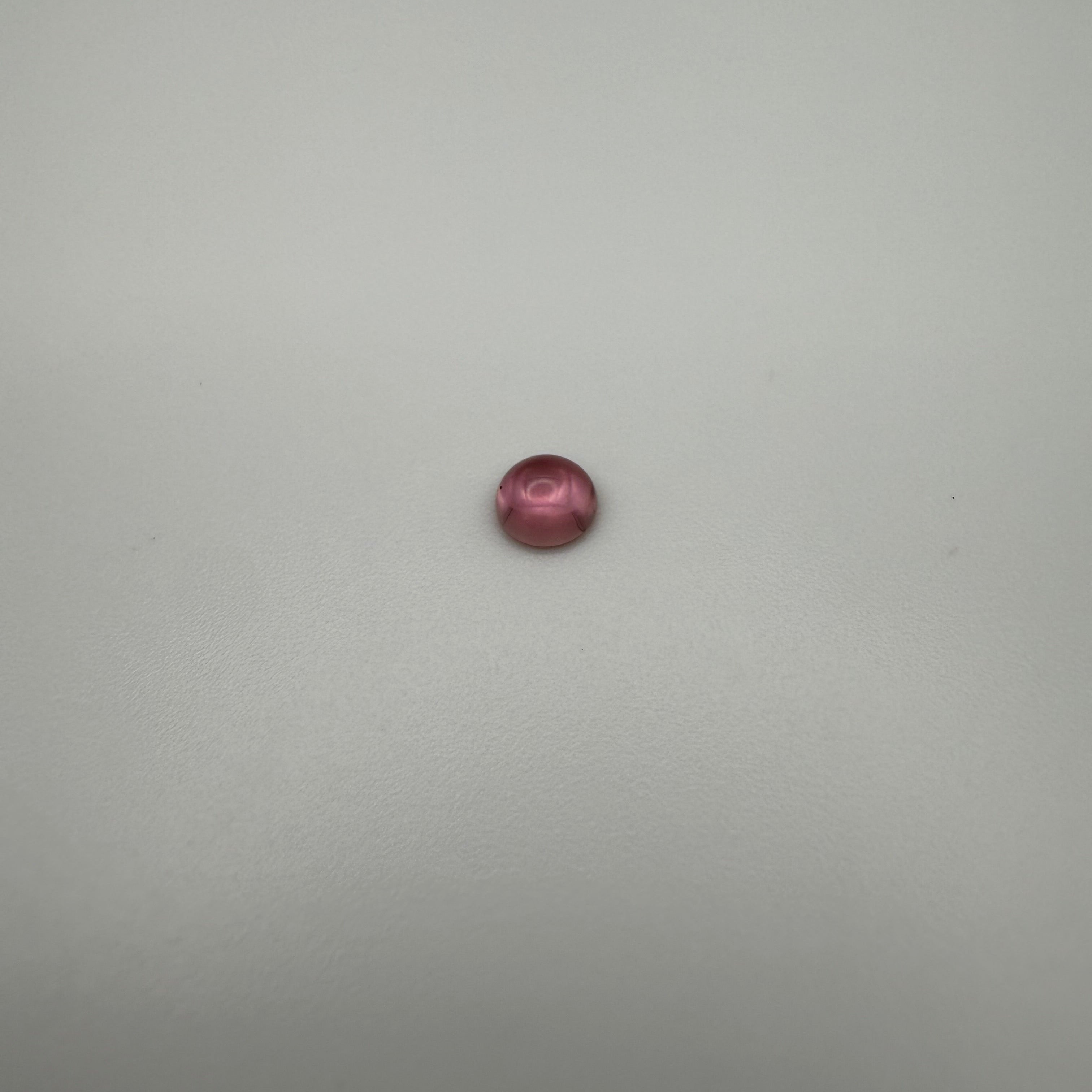 macro view of a pink tourmaline round cabochon on a smooth white surface
