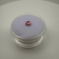 Pink tourmaline round cabochon resting on light purple felt inside a clear gem holder