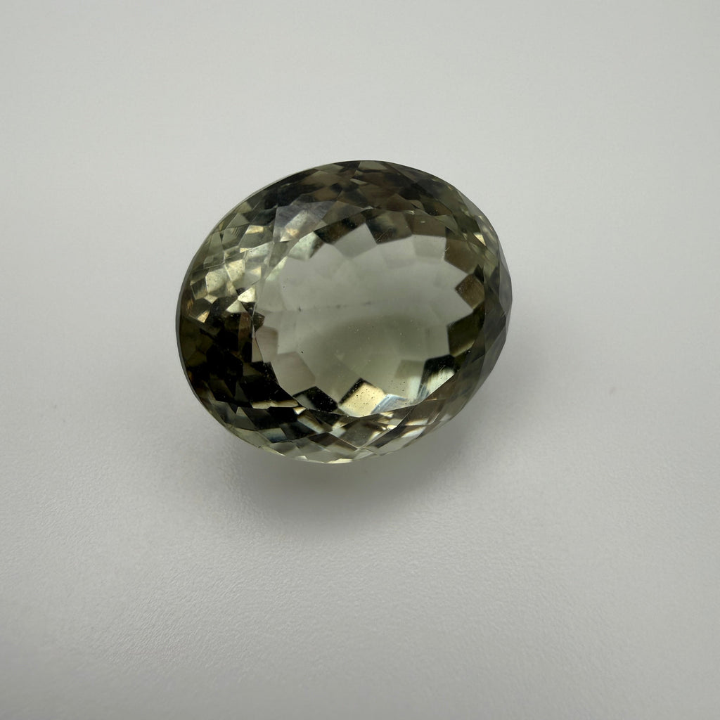 oval faceted pale green prasiolite gemstone resting on a white surface