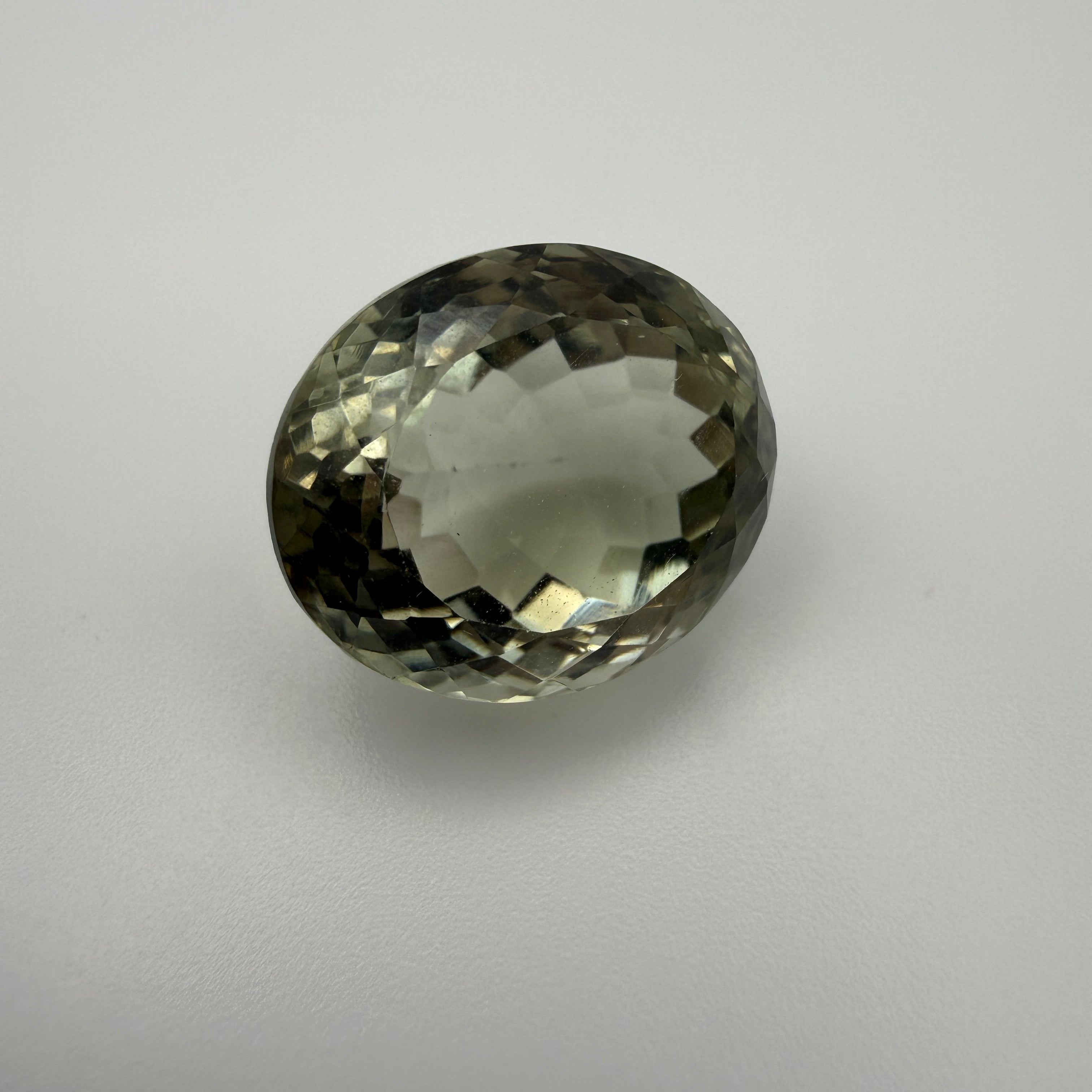 oval faceted pale green prasiolite gemstone resting on a white surface
