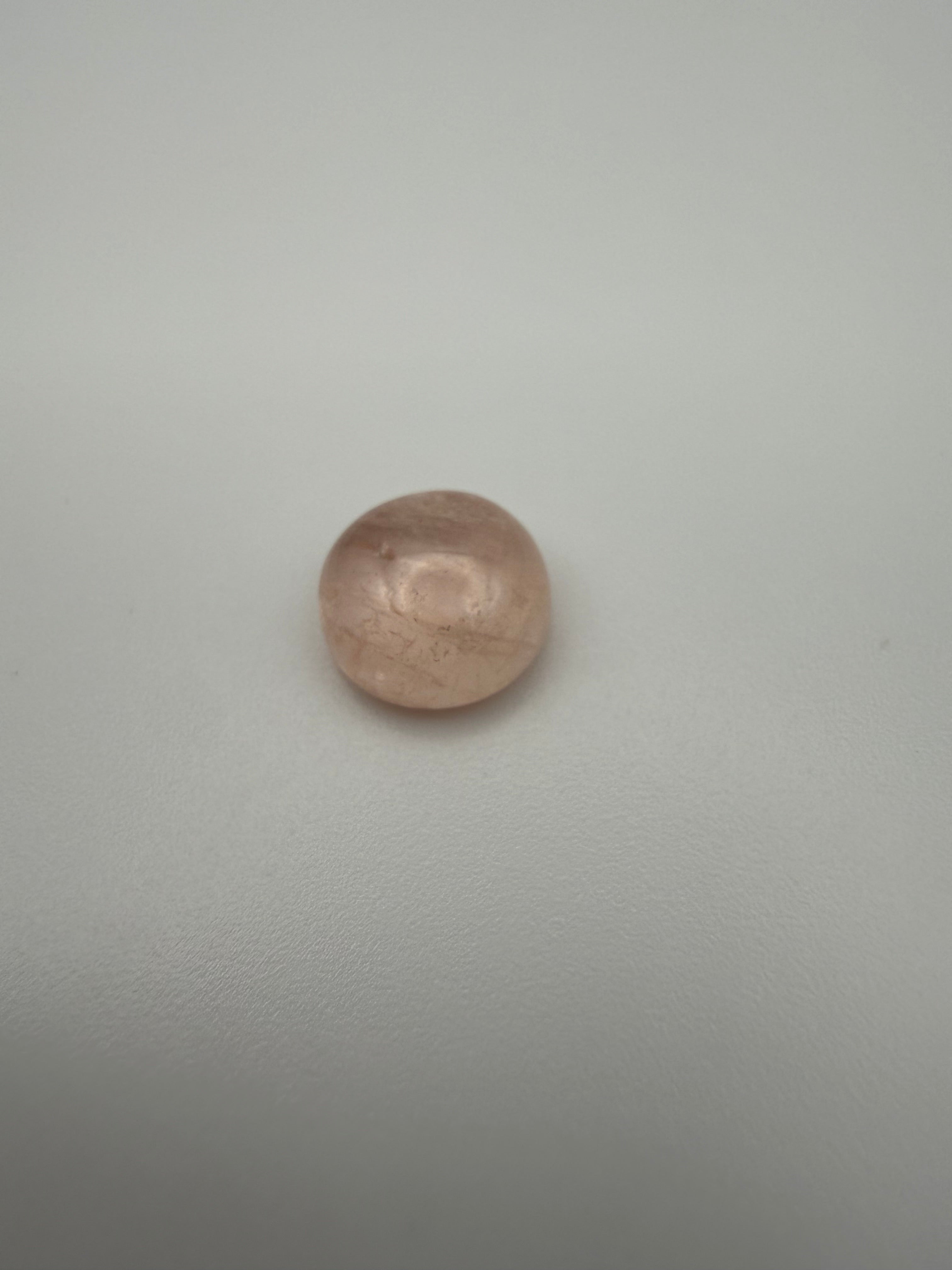 Round peachy-pink morganite cabochon on a smooth white surface