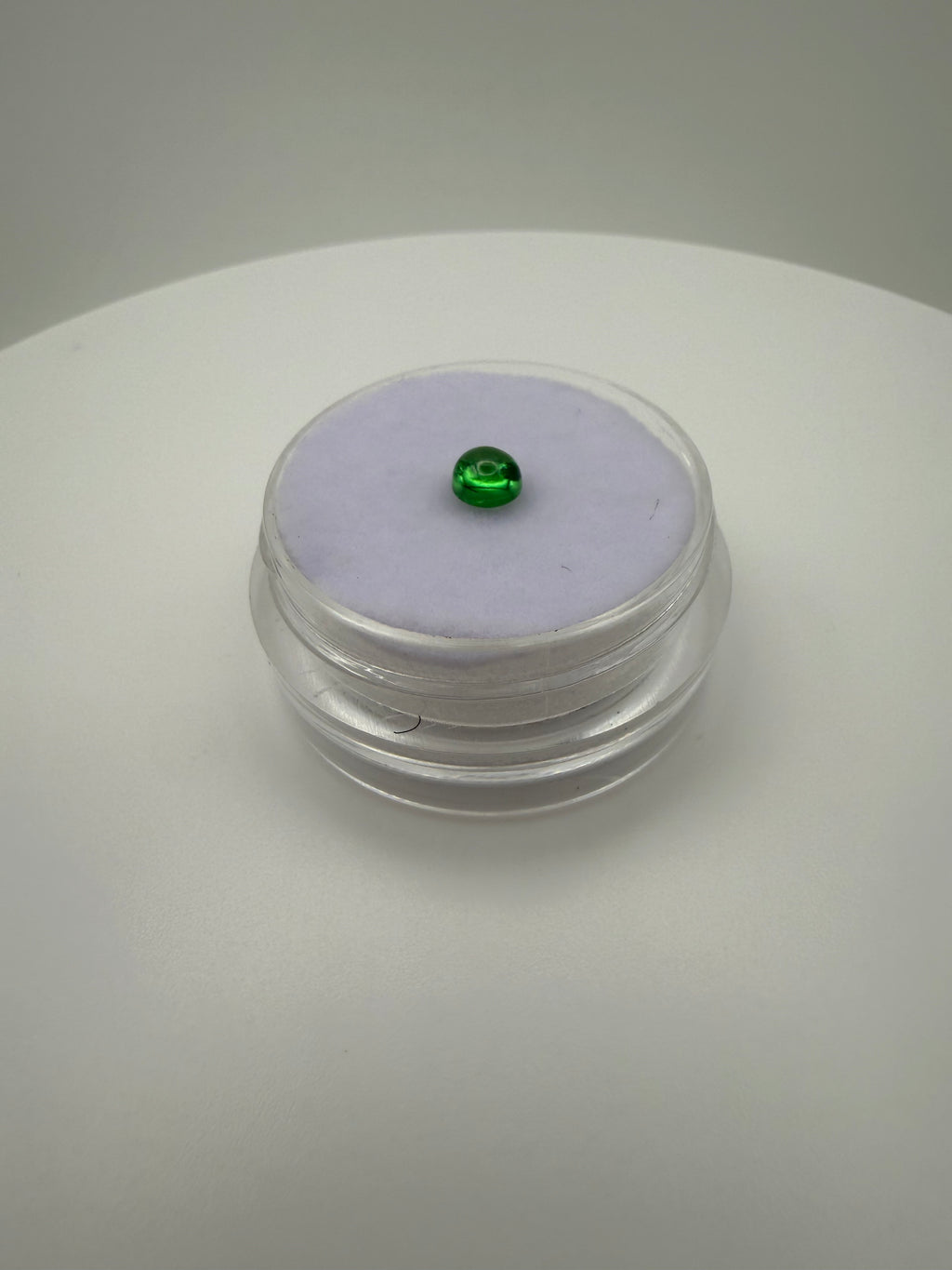Round green cabochon gemstone resting on soft purple fabric in clear holder