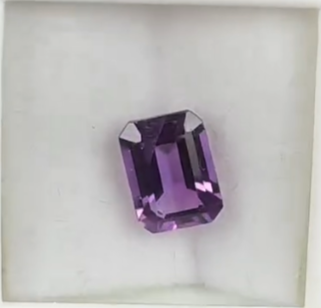 Macro top down view of a 1.44ct violet amethyst rectangular faceted gemstone on a white background.