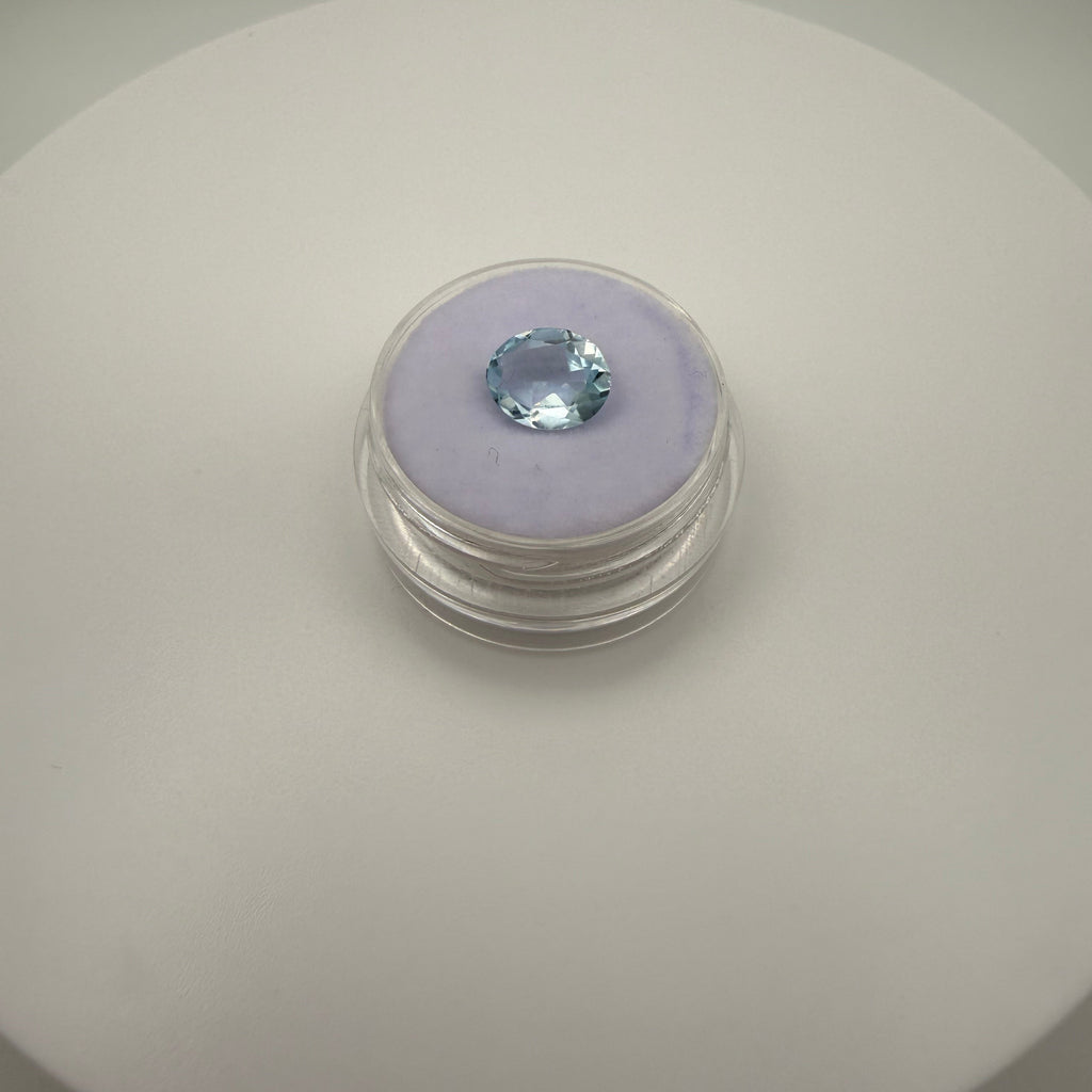 Oval faceted 1.95ct Swiss Blue Topaz gemstone on purple cushion in clear holder