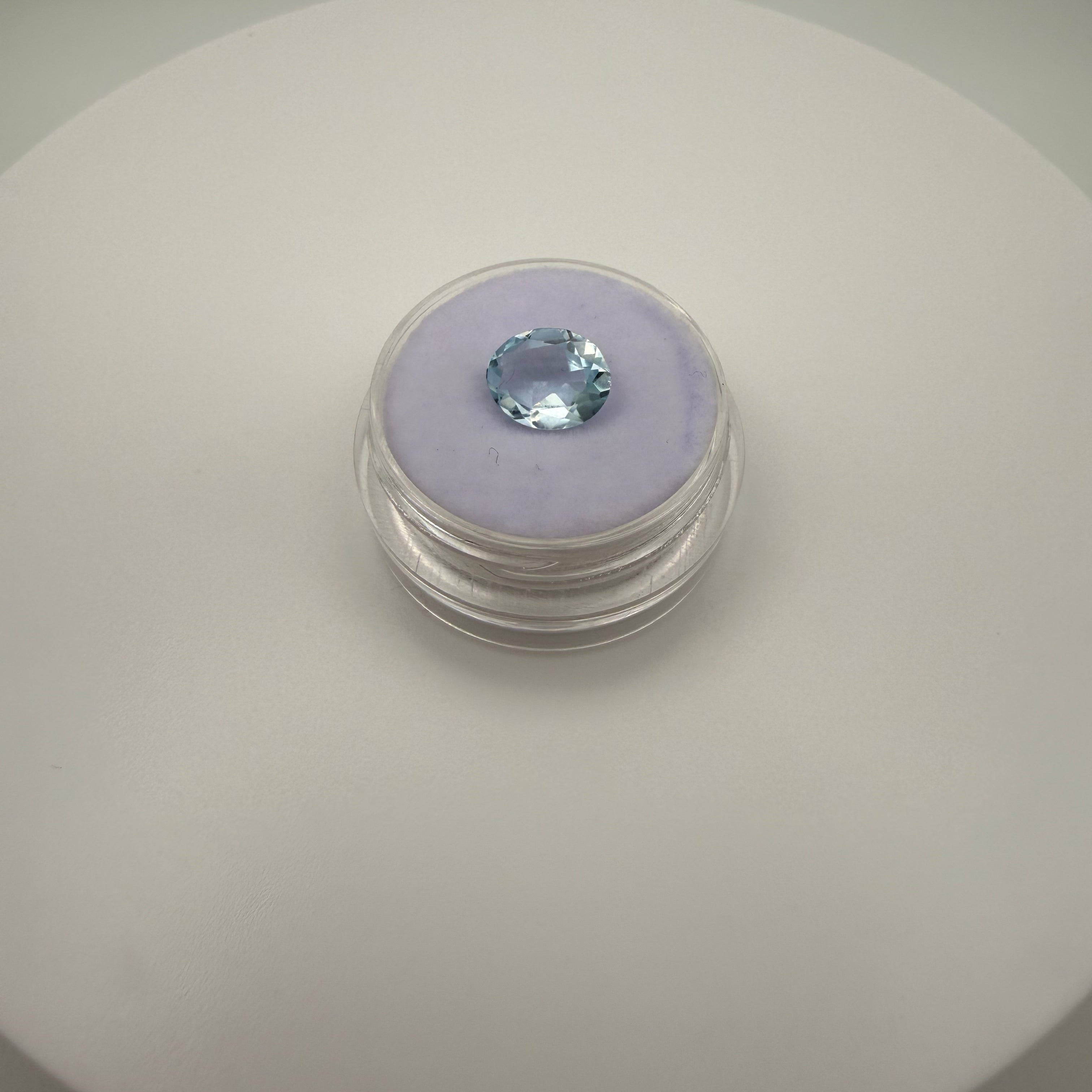 Oval faceted 1.95ct Swiss Blue Topaz gemstone on purple cushion in clear holder