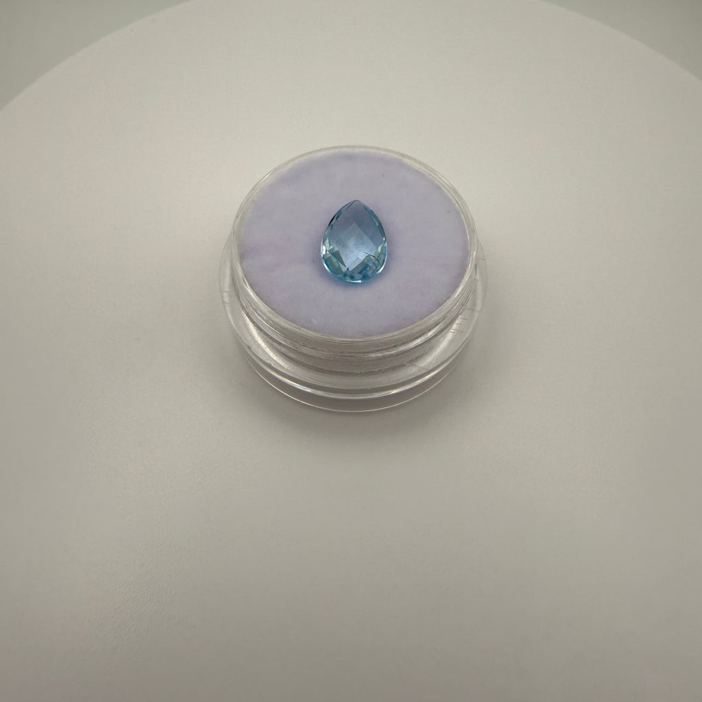 top down view of 2.0ct Swiss Blue Topaz pear faceted gemstone on purple cushion in clear gem holder on white background