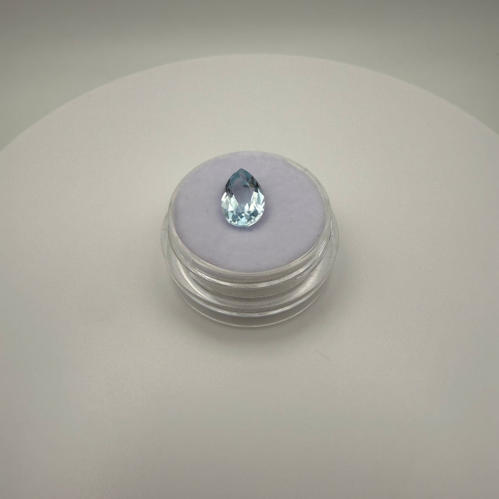 Top-down view of a 2.25ct Swiss Blue Topaz pear faceted gemstone on a soft display surface in a clear gem holder.