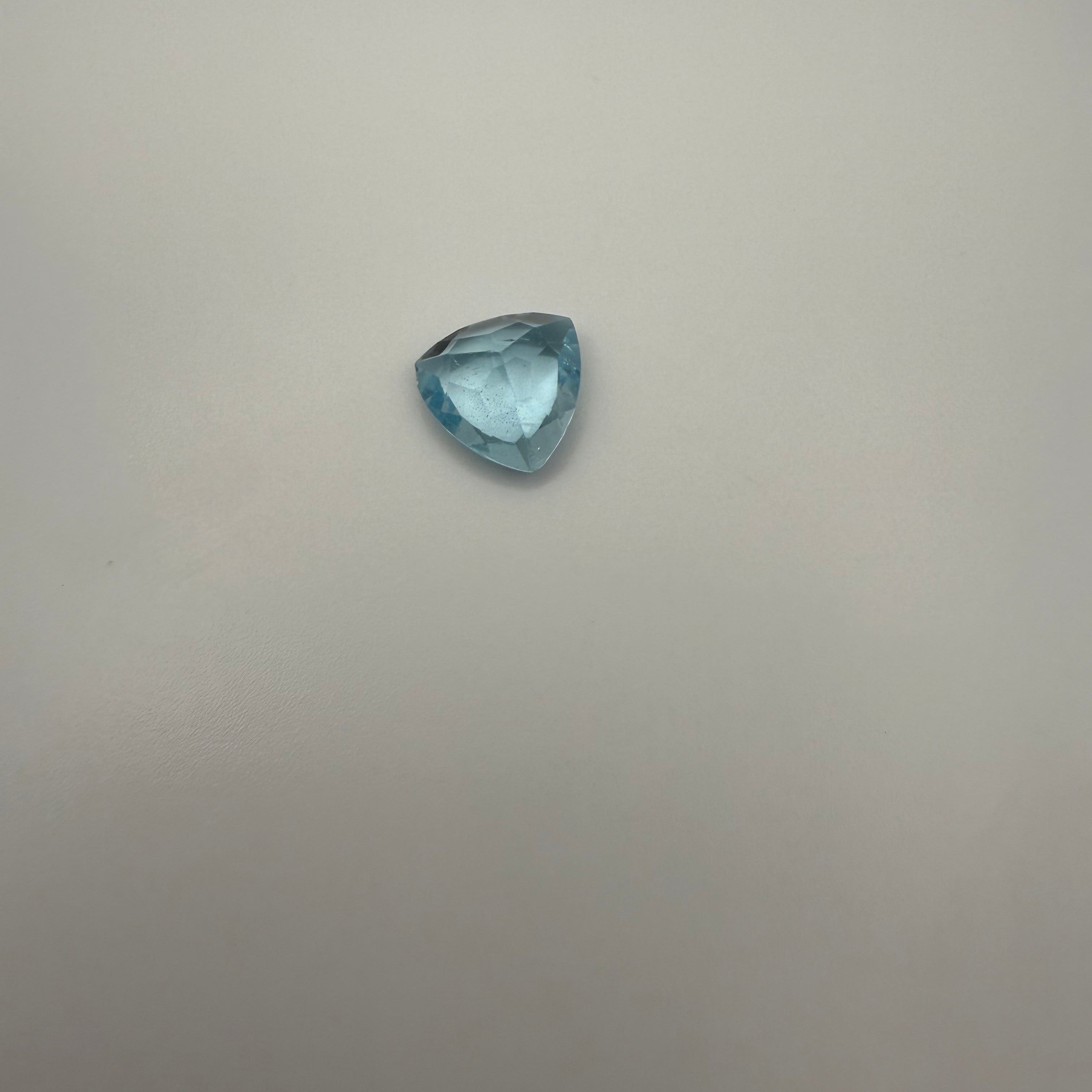 Triangular faceted 3.6ct Swiss Blue Topaz gemstone on a light background