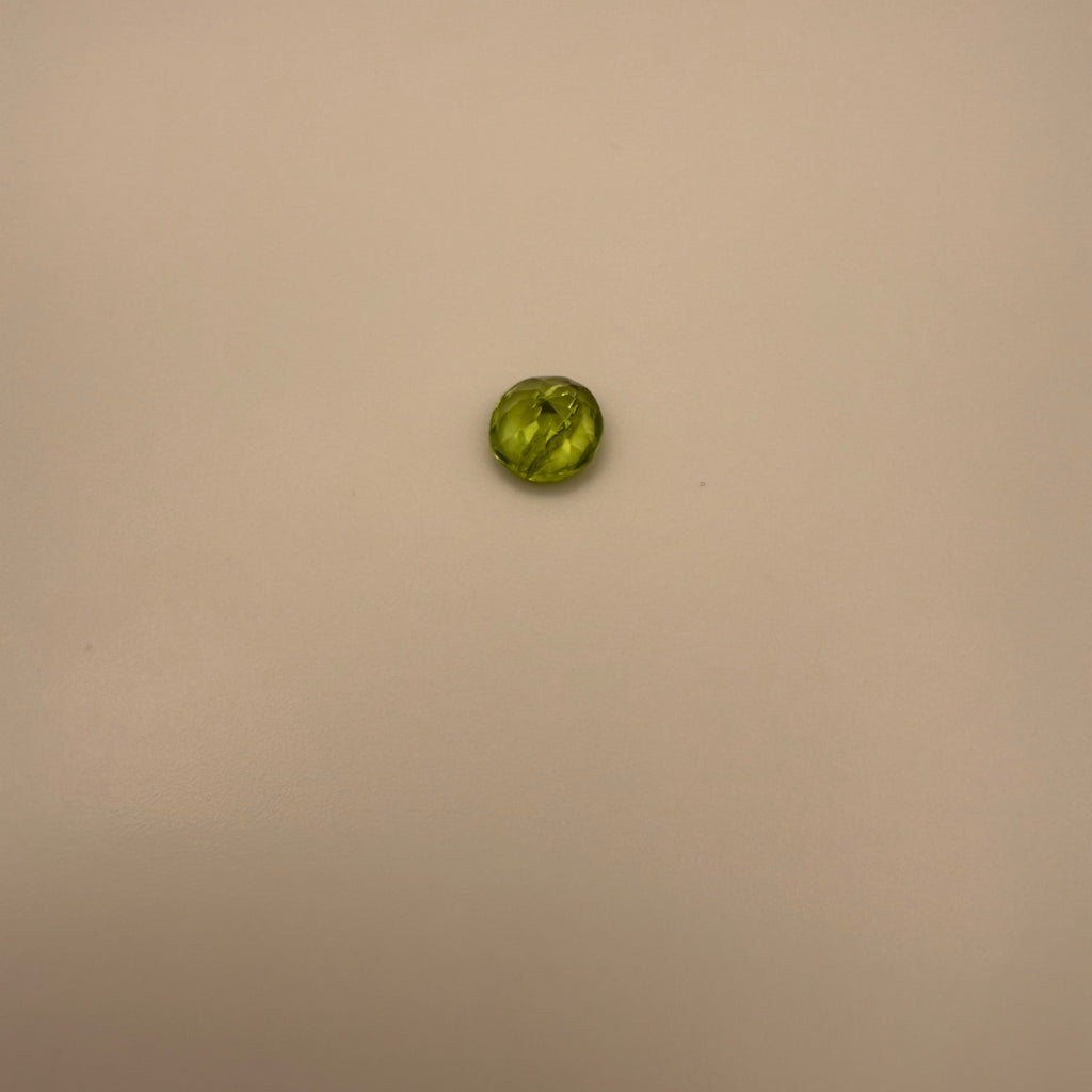 macro top down view of 1.3ct yellow-green peridot round faceted gemstone on a neutral background
