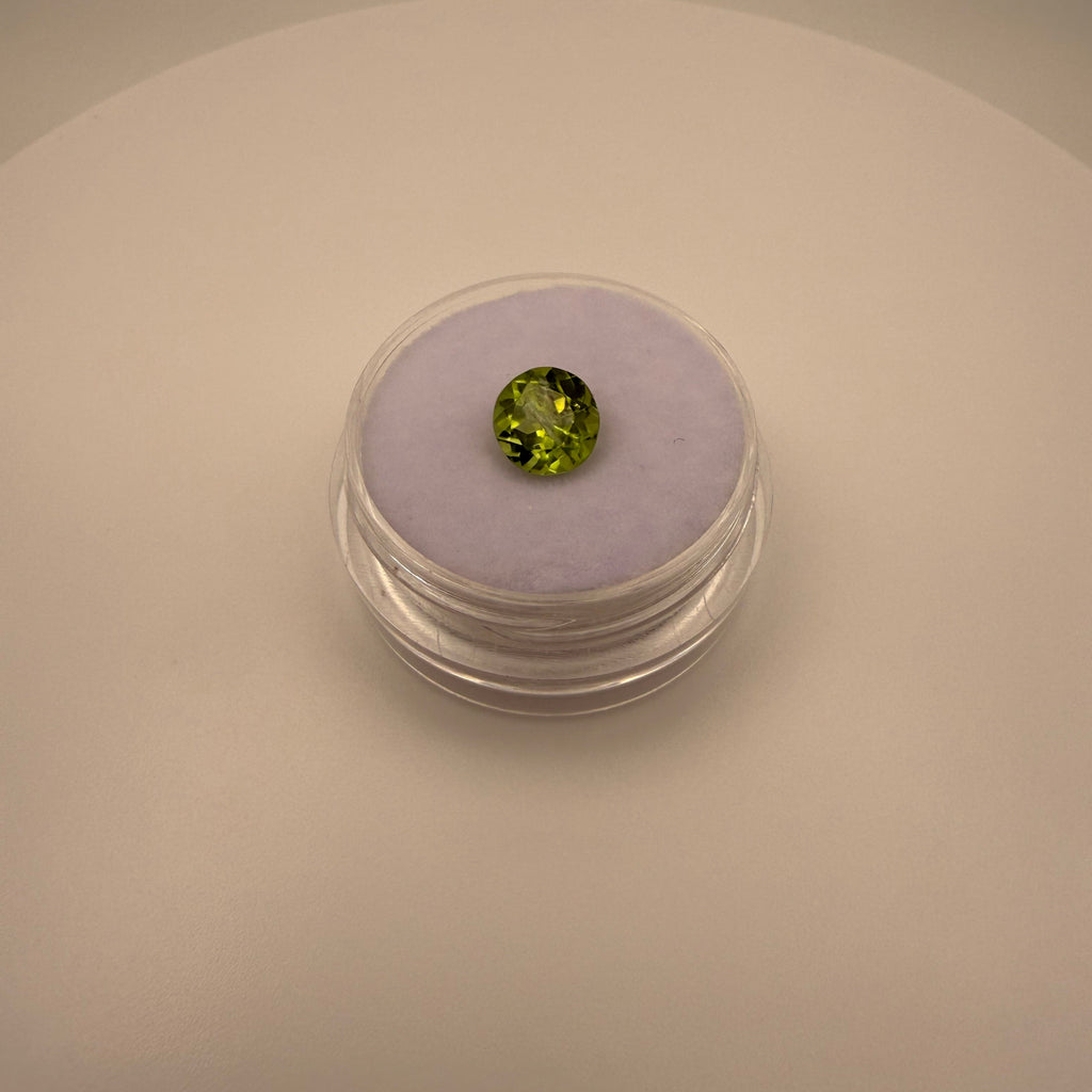 Round faceted 1.3ct yellow-green peridot gemstone on soft lavender holder