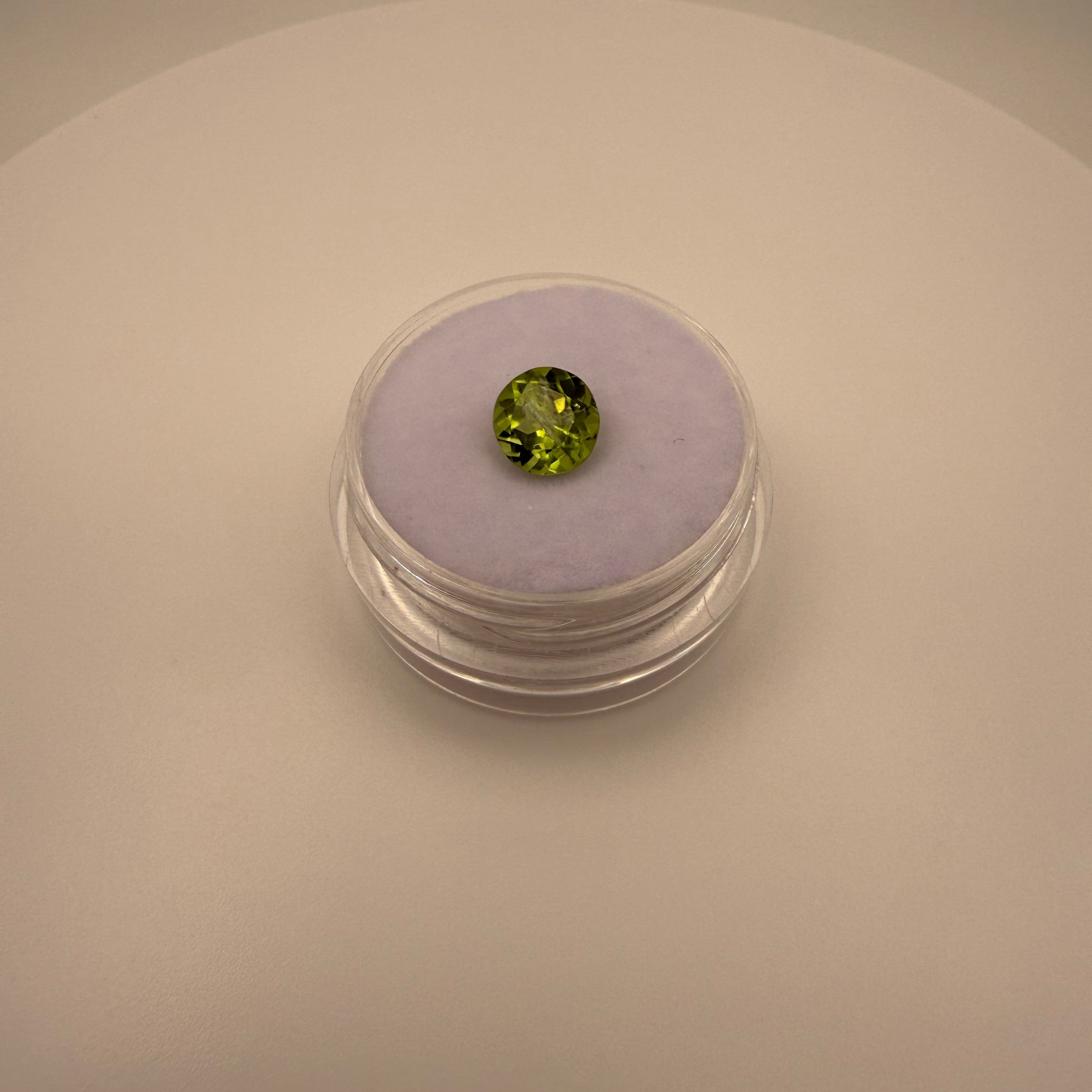 Round faceted 1.3ct yellow-green peridot gemstone on soft lavender holder