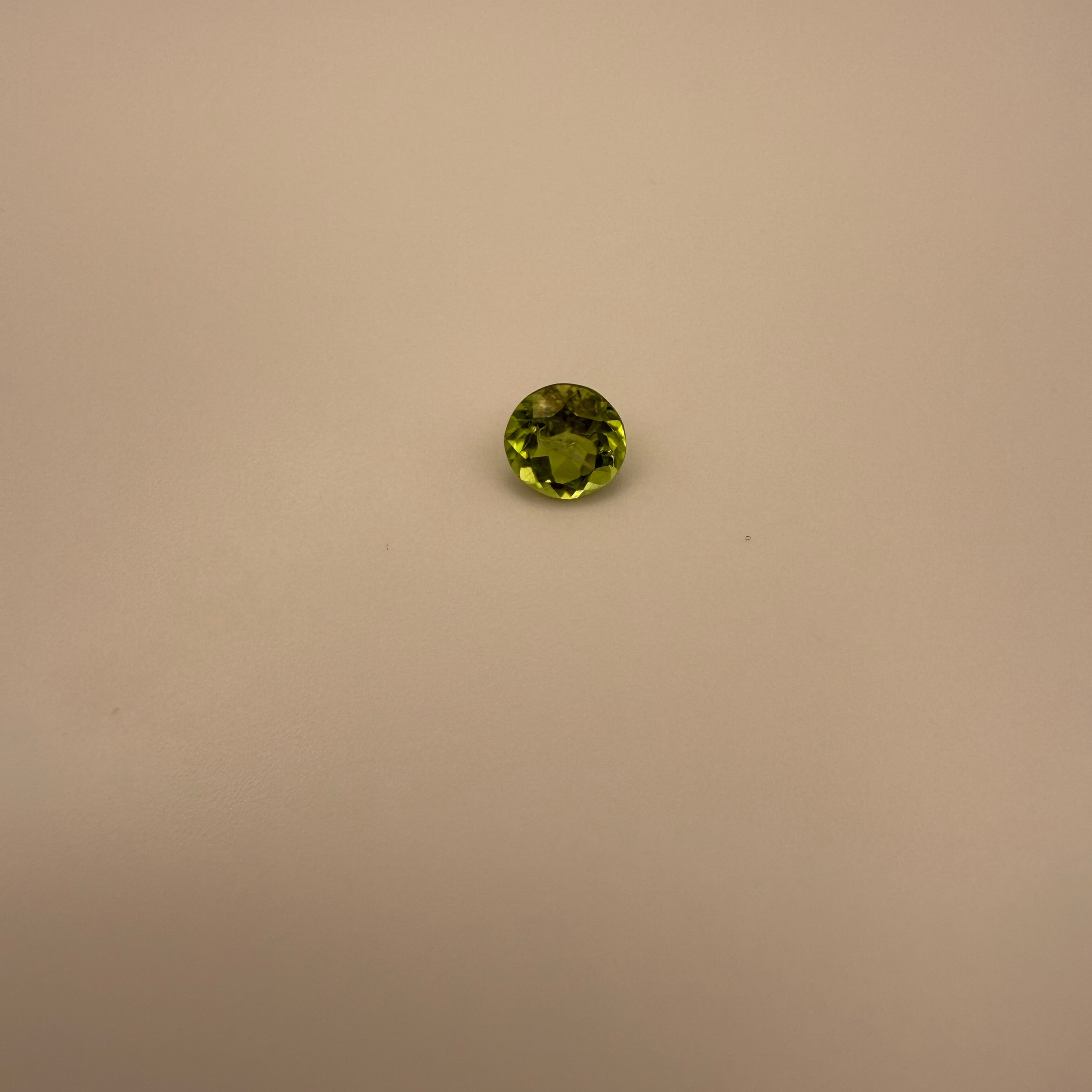 Round faceted 1.3ct yellow-green peridot gemstone on a light background
