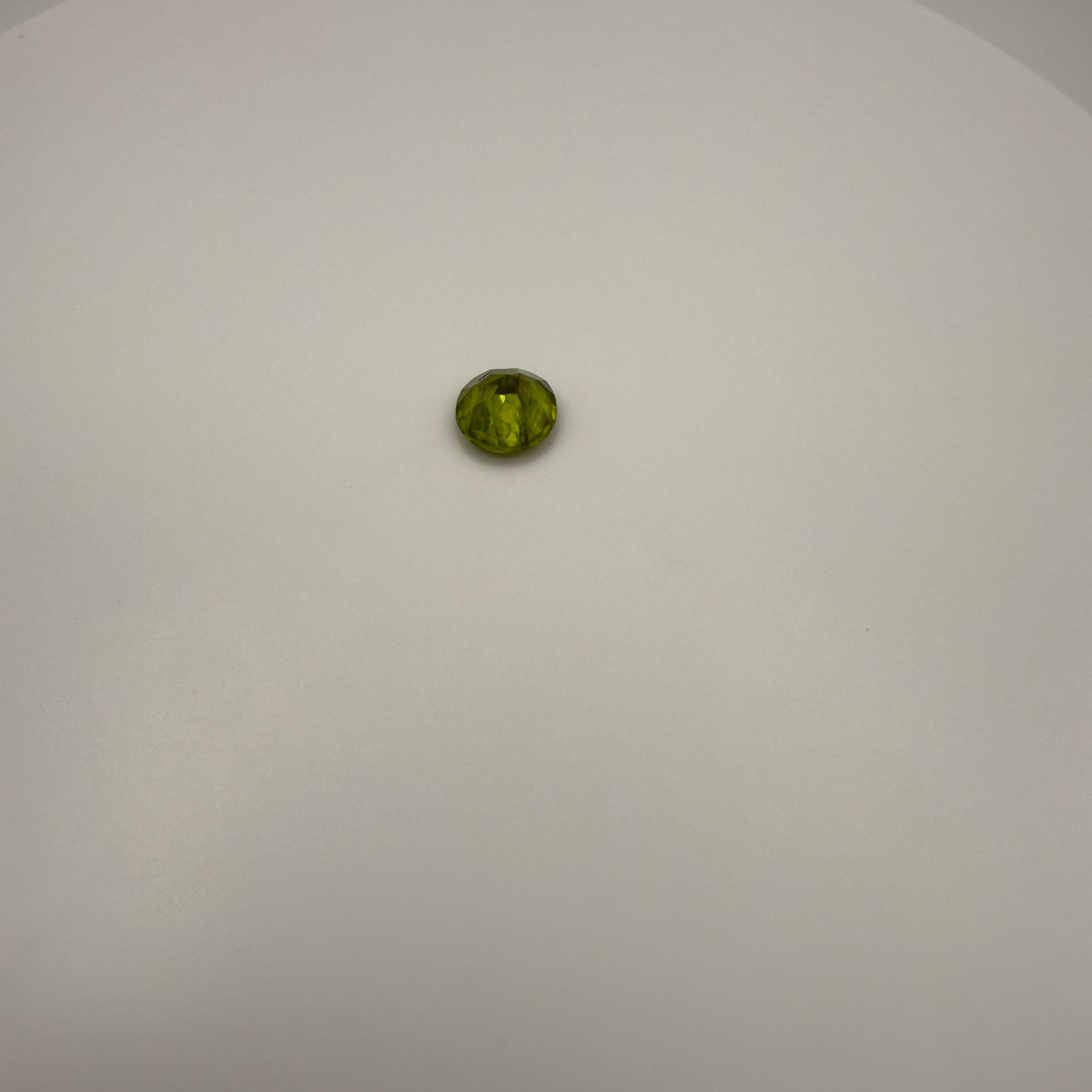 round faceted 1.8ct yellow-green peridot gemstone on a light background