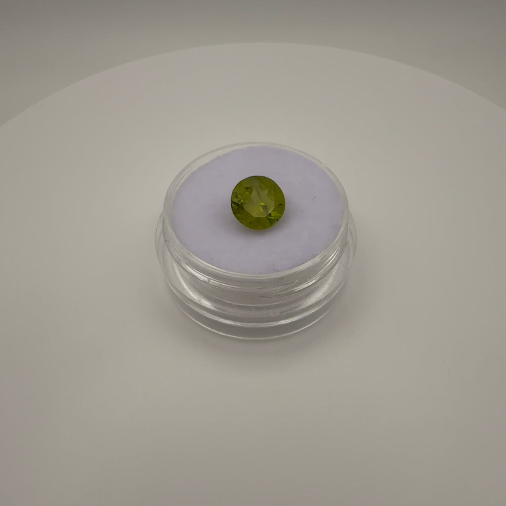 macro top down view of 1.8ct yellow-green peridot round faceted gemstone in clear holder on white surface
