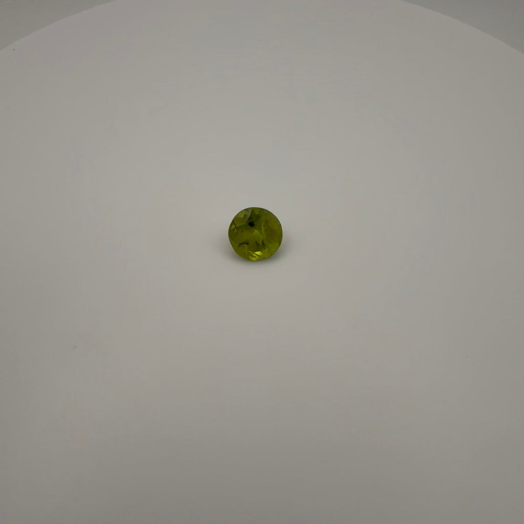 macro top down view of 1.8ct round faceted yellow-green peridot gemstone on a white background