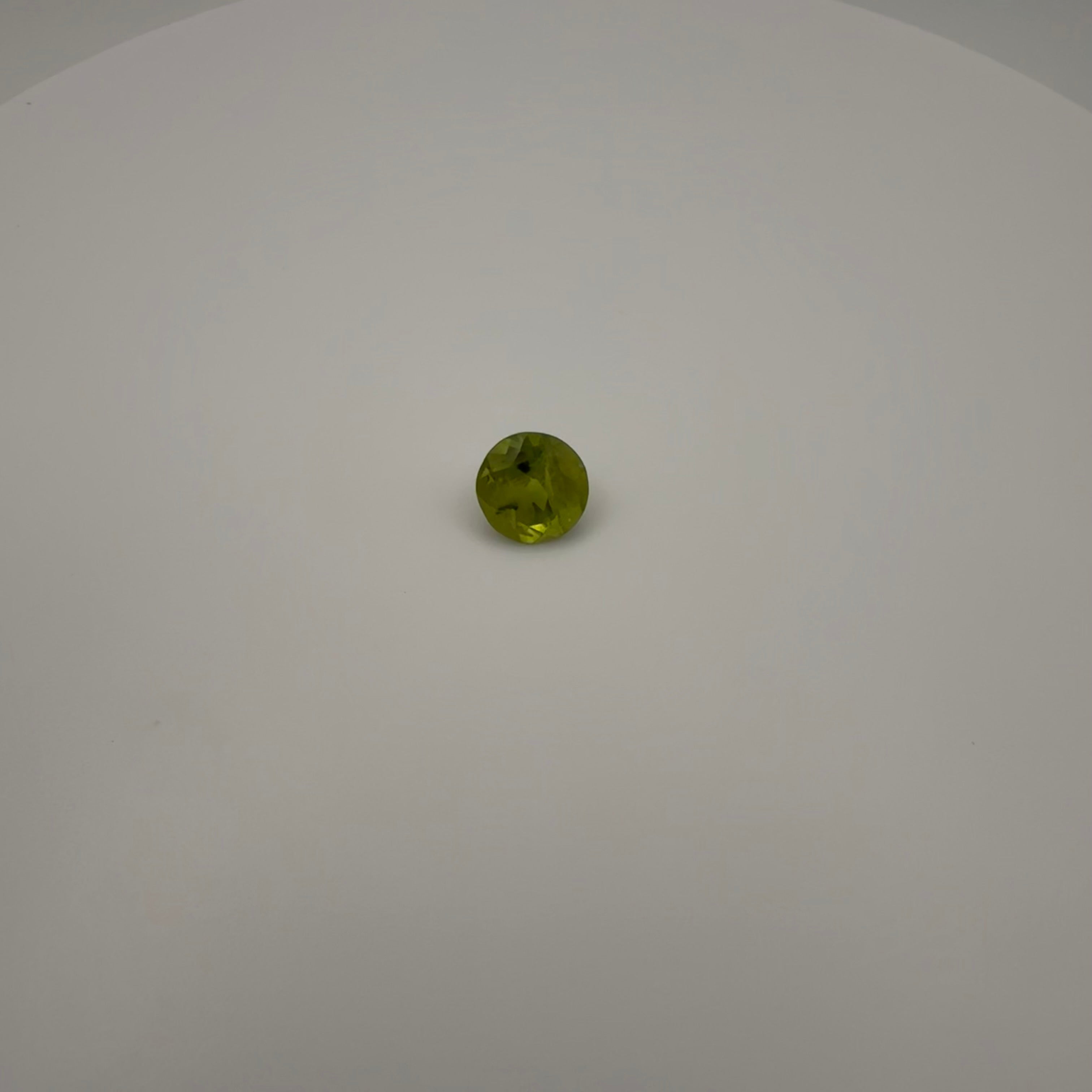 macro top down view of 1.8ct round faceted yellow-green peridot gemstone on a white background