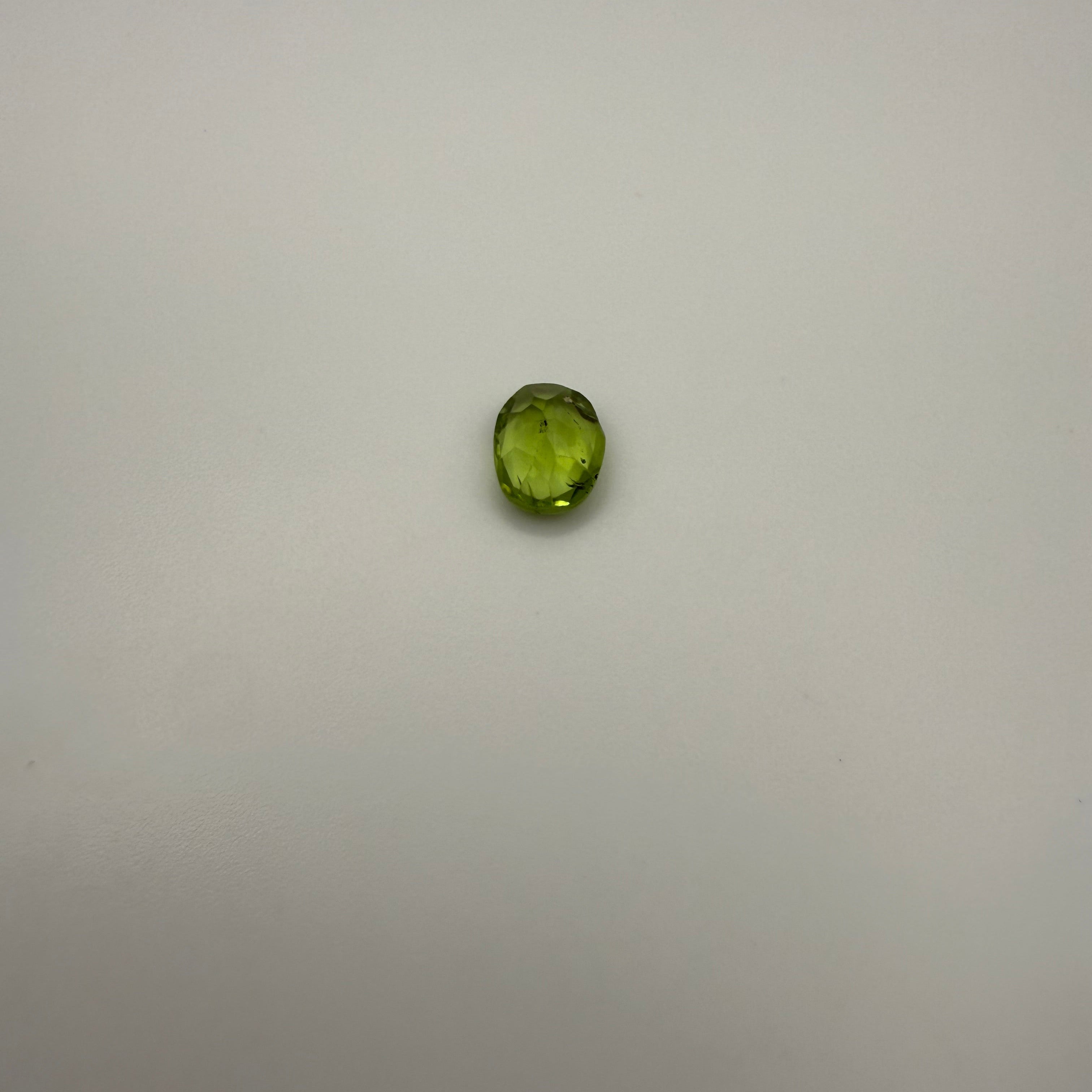 oval faceted 1.25ct yellow-green peridot gemstone on a plain background
