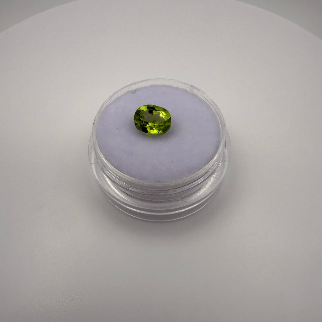 1.25ct oval faceted yellow-green peridot gemstone resting on a light-colored cushion in a round transparent gem holder.