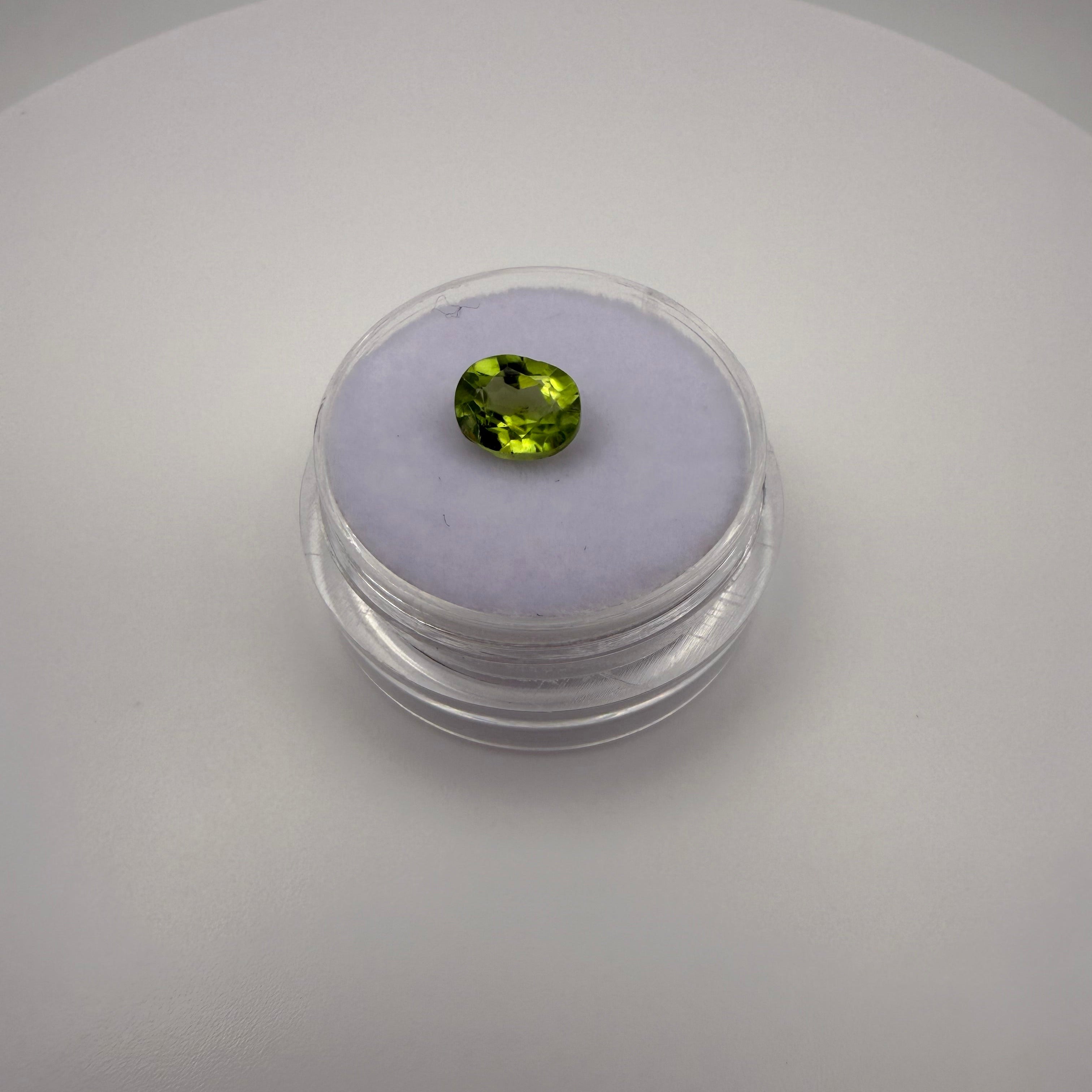 1.25ct oval faceted yellow-green peridot gemstone resting on a light-colored cushion in a round transparent gem holder.