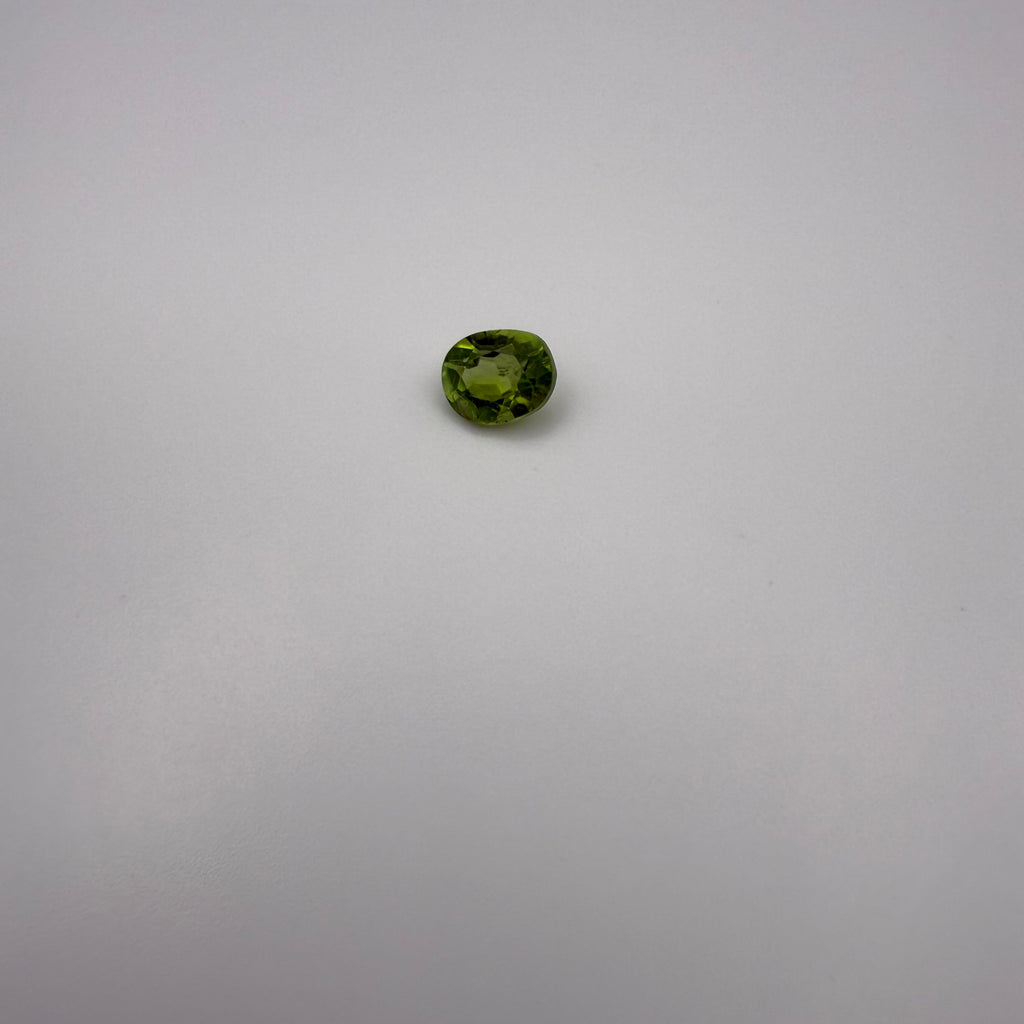 oval faceted 1.25ct yellow-green peridot gemstone on a light background