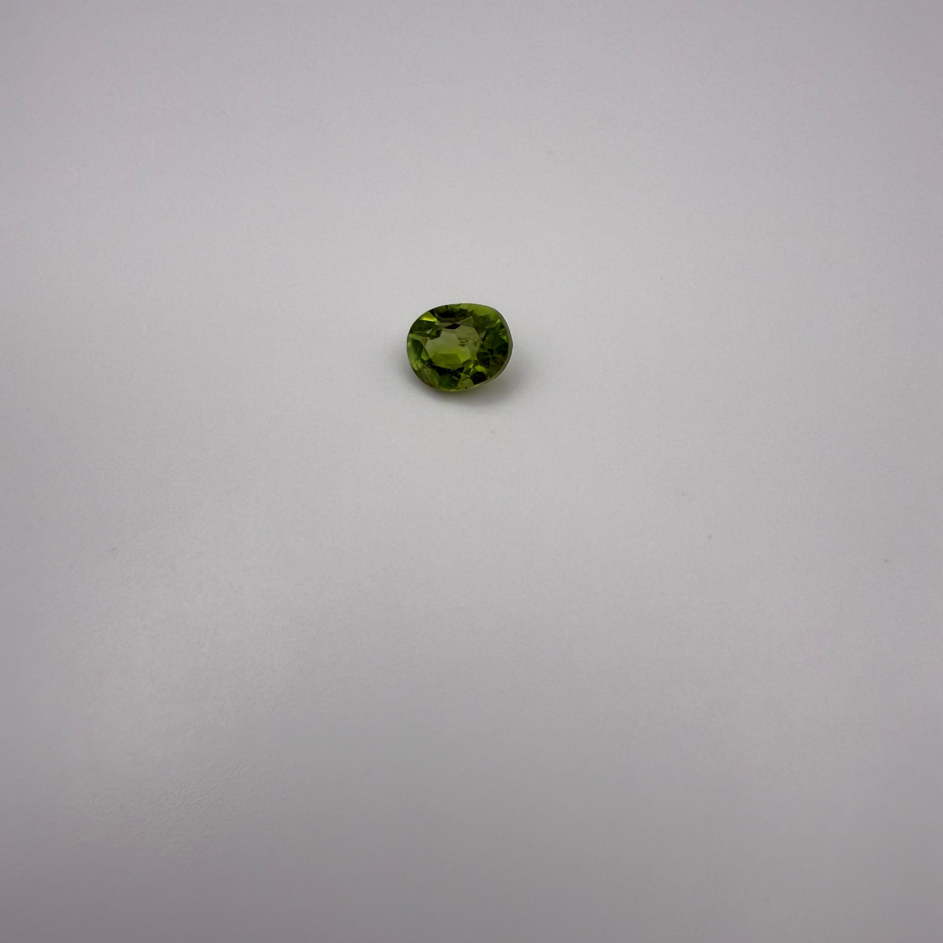 oval faceted 1.25ct yellow-green peridot gemstone on a light background