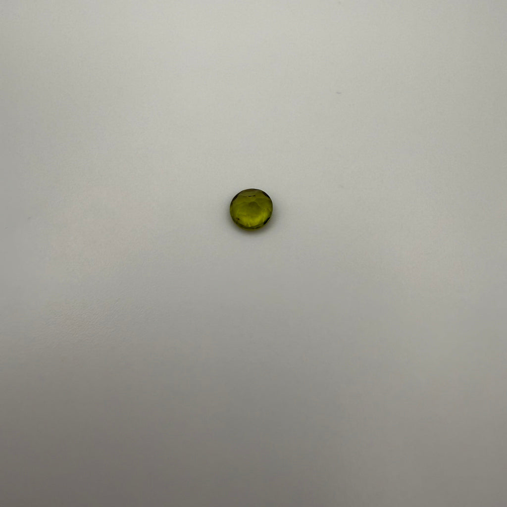 macro top down view of 0.45ct yellow-green peridot round faceted gemstone on a smooth light background