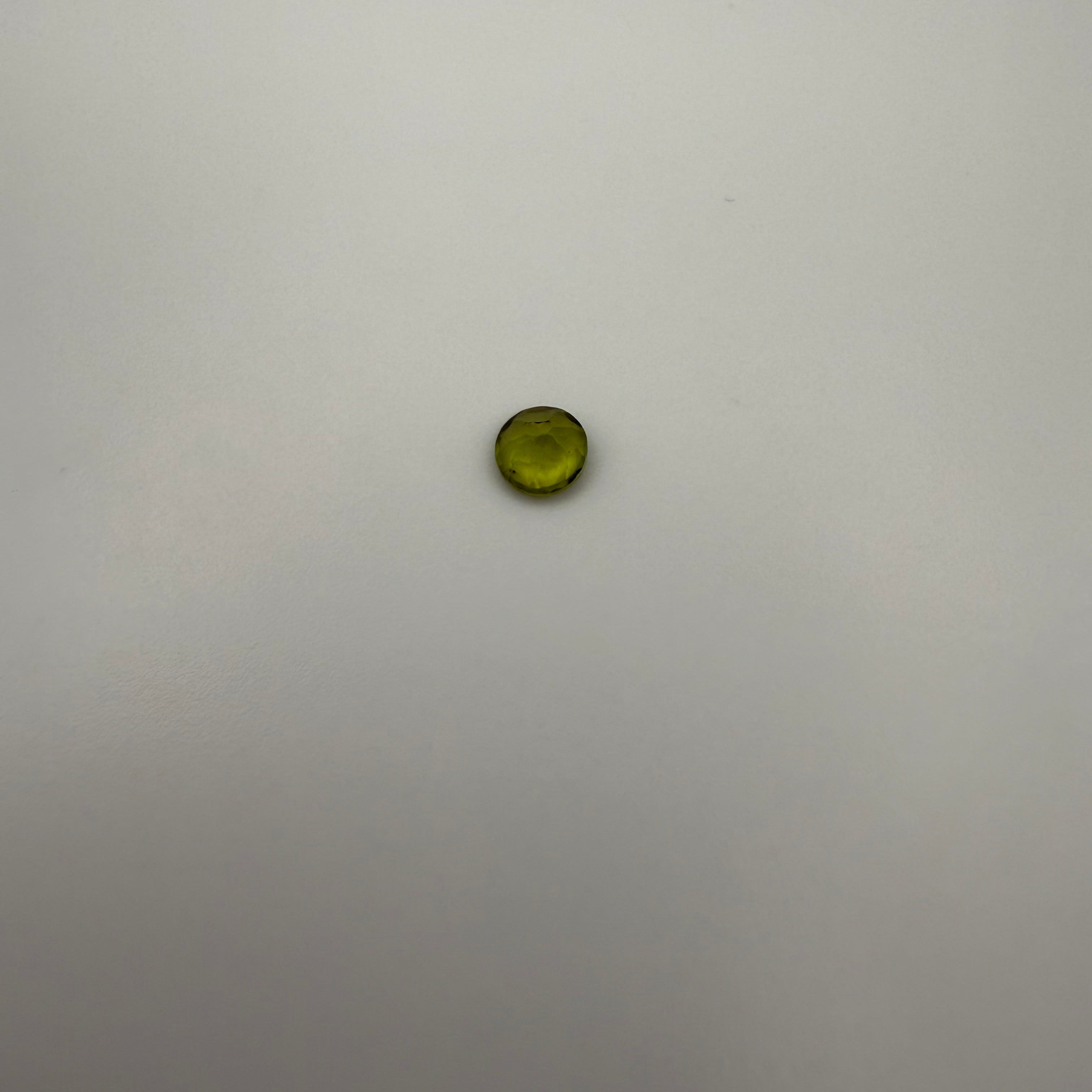 macro top down view of 0.45ct yellow-green peridot round faceted gemstone on a smooth light background