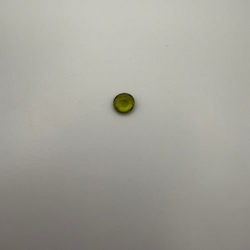macro top down view of 0.45ct yellow-green peridot round faceted gemstone on a smooth light background