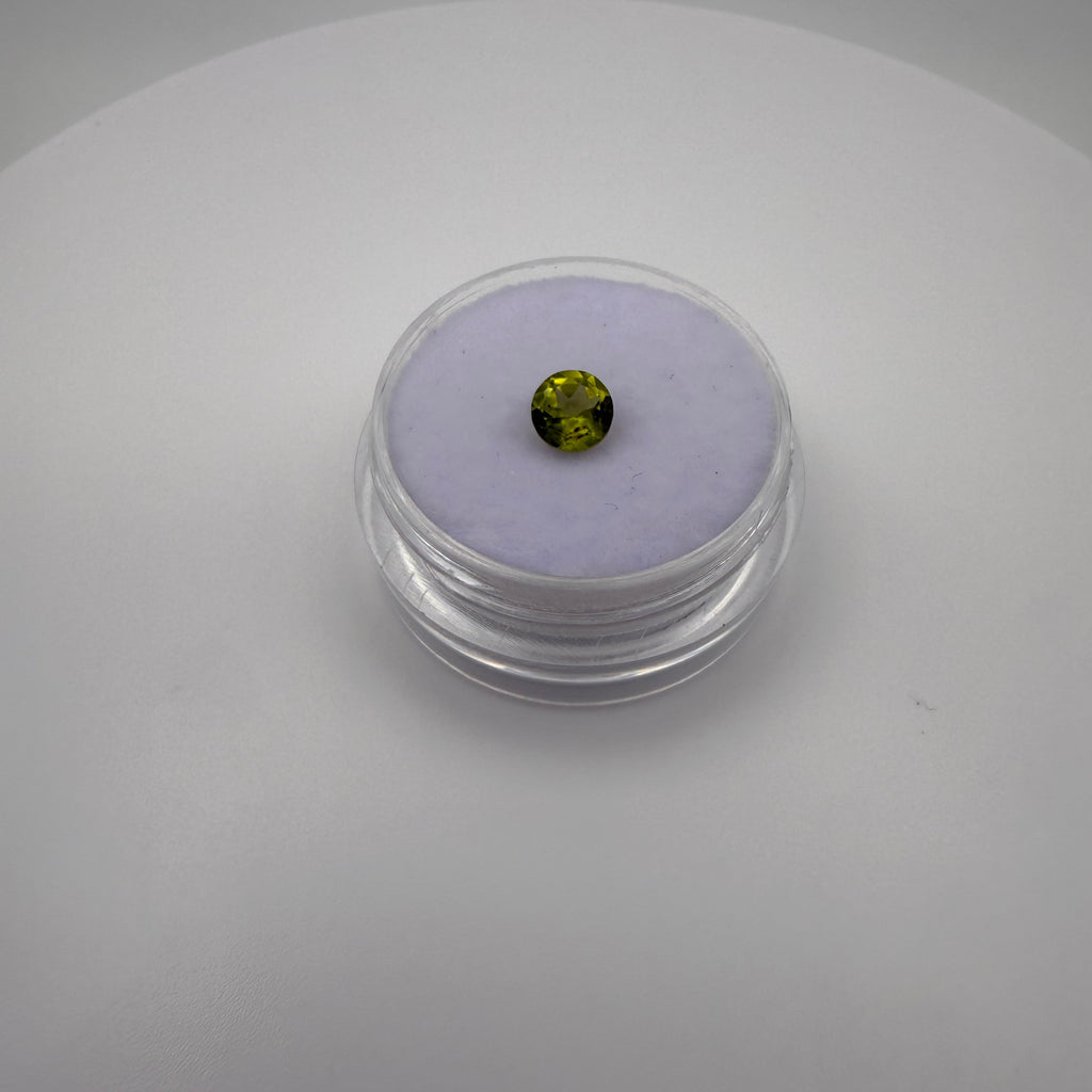 macro top view of 0.45ct yellow-green peridot round faceted gemstone in a clear holder on purple cushion backdrop