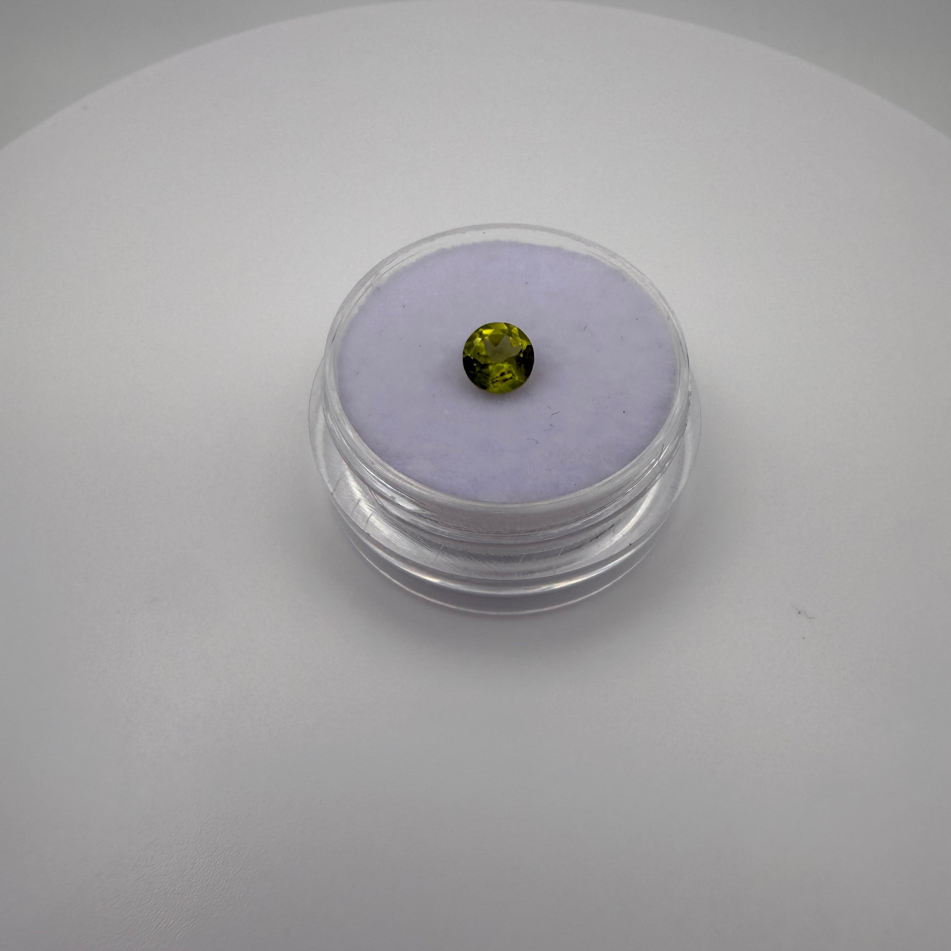 macro top view of 0.45ct yellow-green peridot round faceted gemstone in a clear holder on purple cushion backdrop