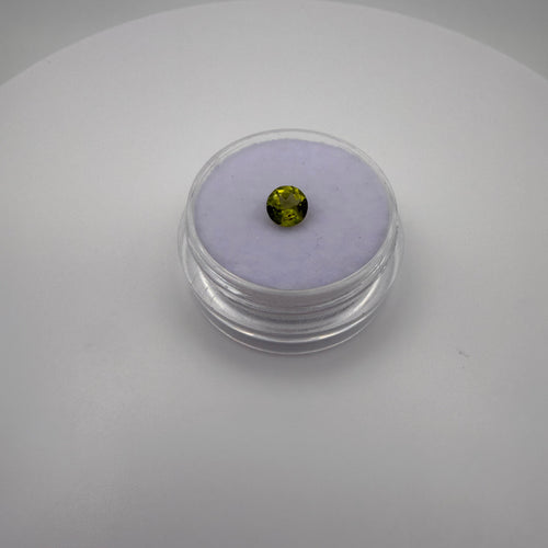 macro top view of 0.45ct yellow-green peridot round faceted gemstone in a clear holder on purple cushion backdrop