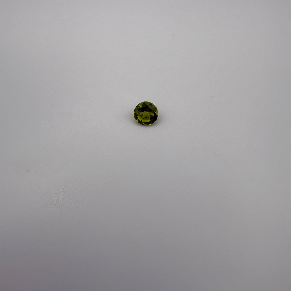 Macro view of a 0.45ct yellow-green round faceted peridot gemstone on a white background.