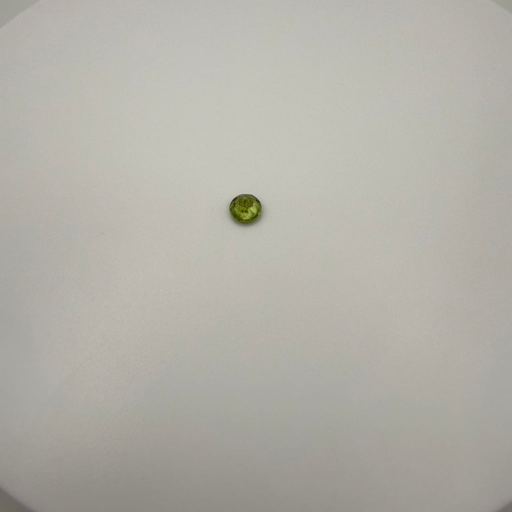 top-down view of a 0.45ct yellow-green peridot round faceted gemstone on a white surface