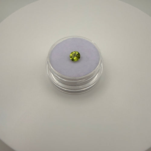 Macro top-down view of a 0.45ct yellow-green peridot round faceted gemstone on a soft purple cushion in a clear gem holder.