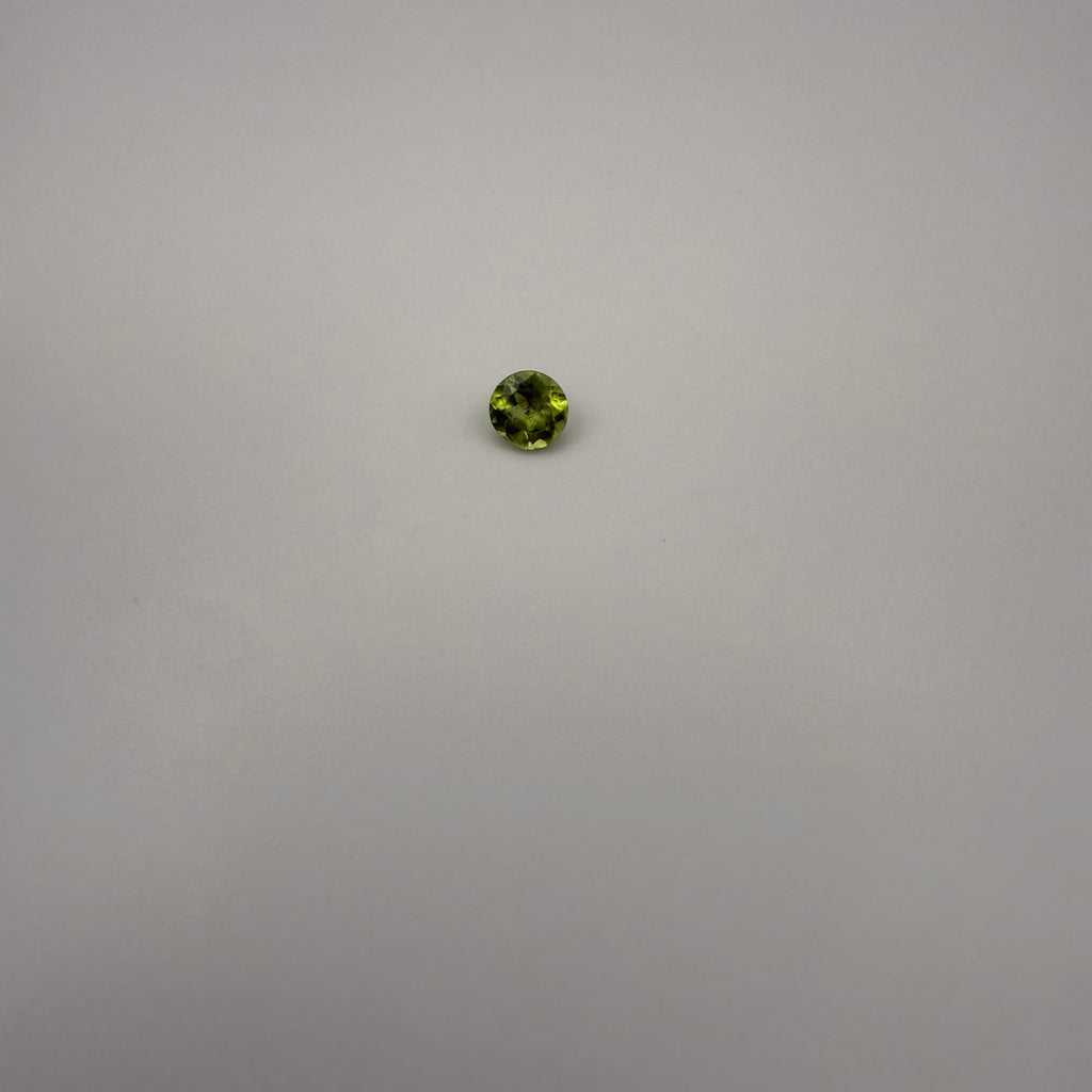 Round faceted 0.45ct yellow-green peridot gemstone on a light background
