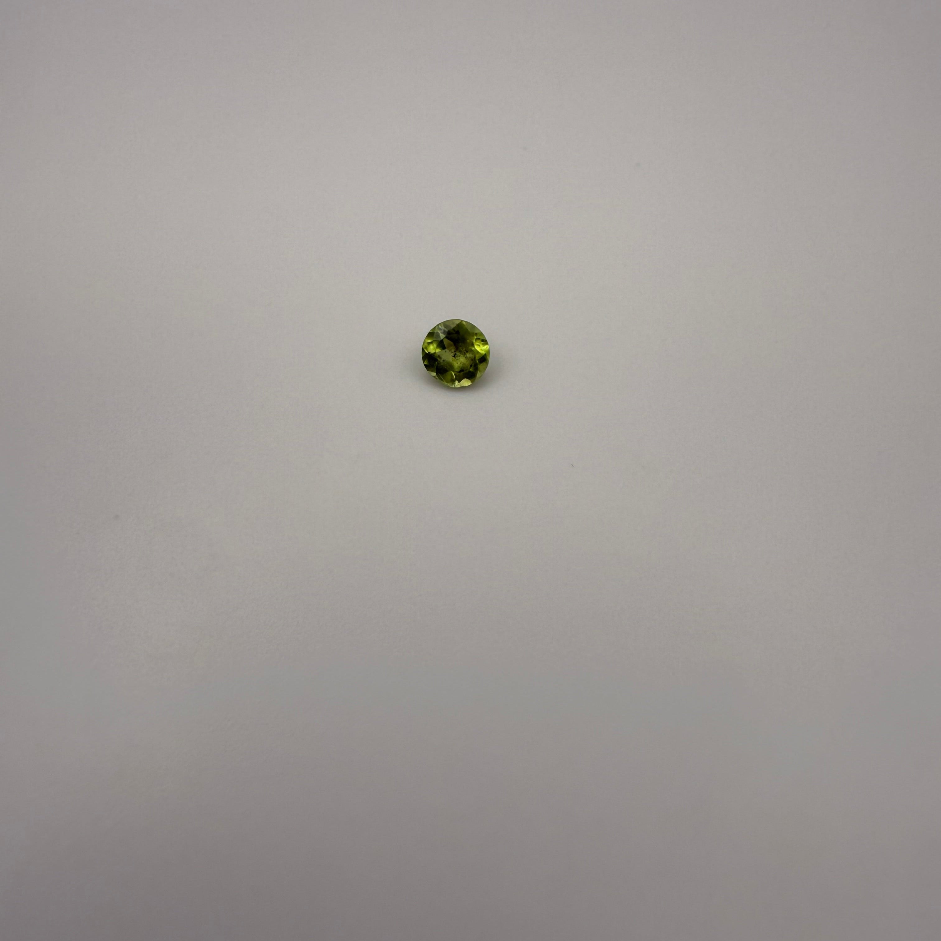 Round faceted 0.45ct yellow-green peridot gemstone on a light background