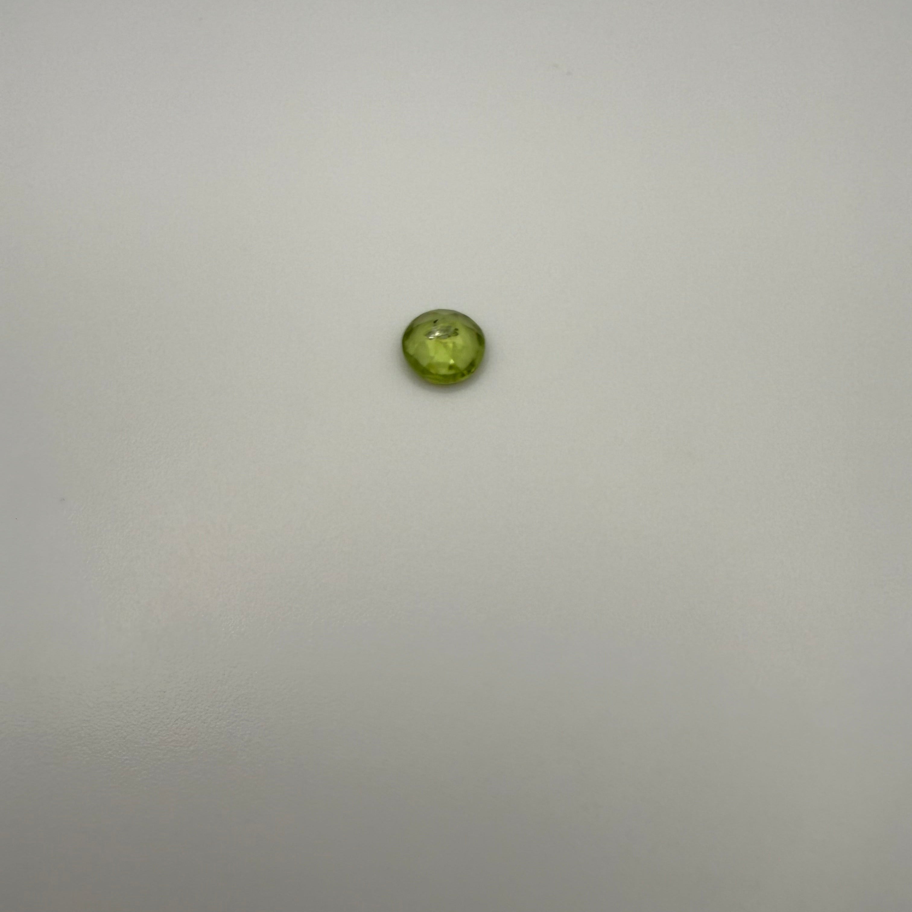 0.5ct round faceted yellow-green peridot gemstone on a smooth light background
