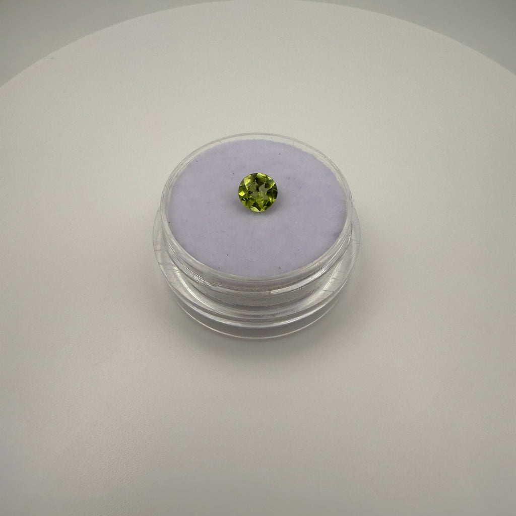 Macro view of 0.5ct yellow-green peridot round faceted gemstone on a soft purple cushion inside a clear gem holder.