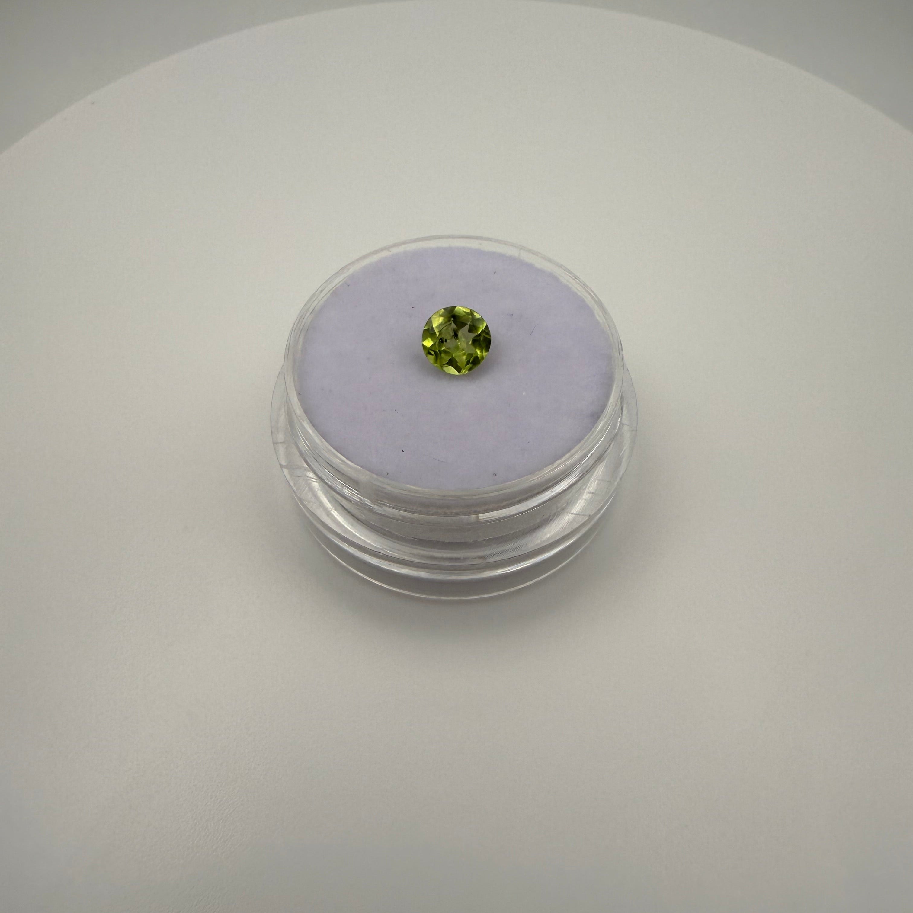 Macro view of 0.5ct yellow-green peridot round faceted gemstone on a soft purple cushion inside a clear gem holder.