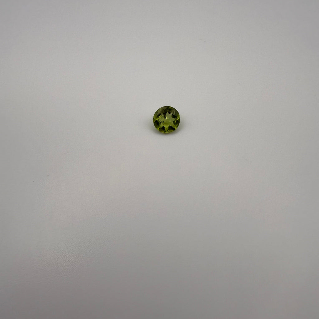 Round faceted 0.5ct yellow-green peridot gemstone on a smooth light background