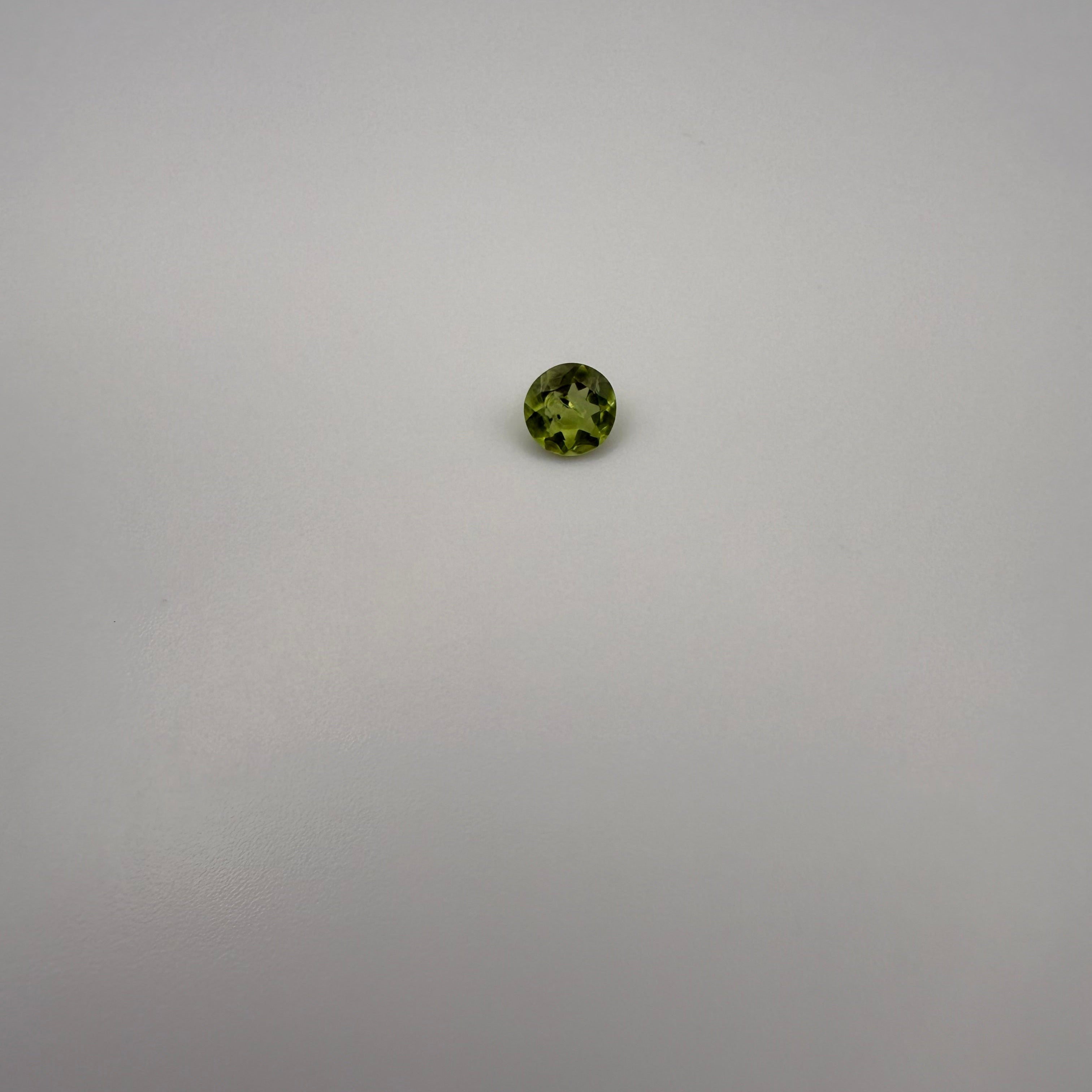 Round faceted 0.5ct yellow-green peridot gemstone on a smooth light background
