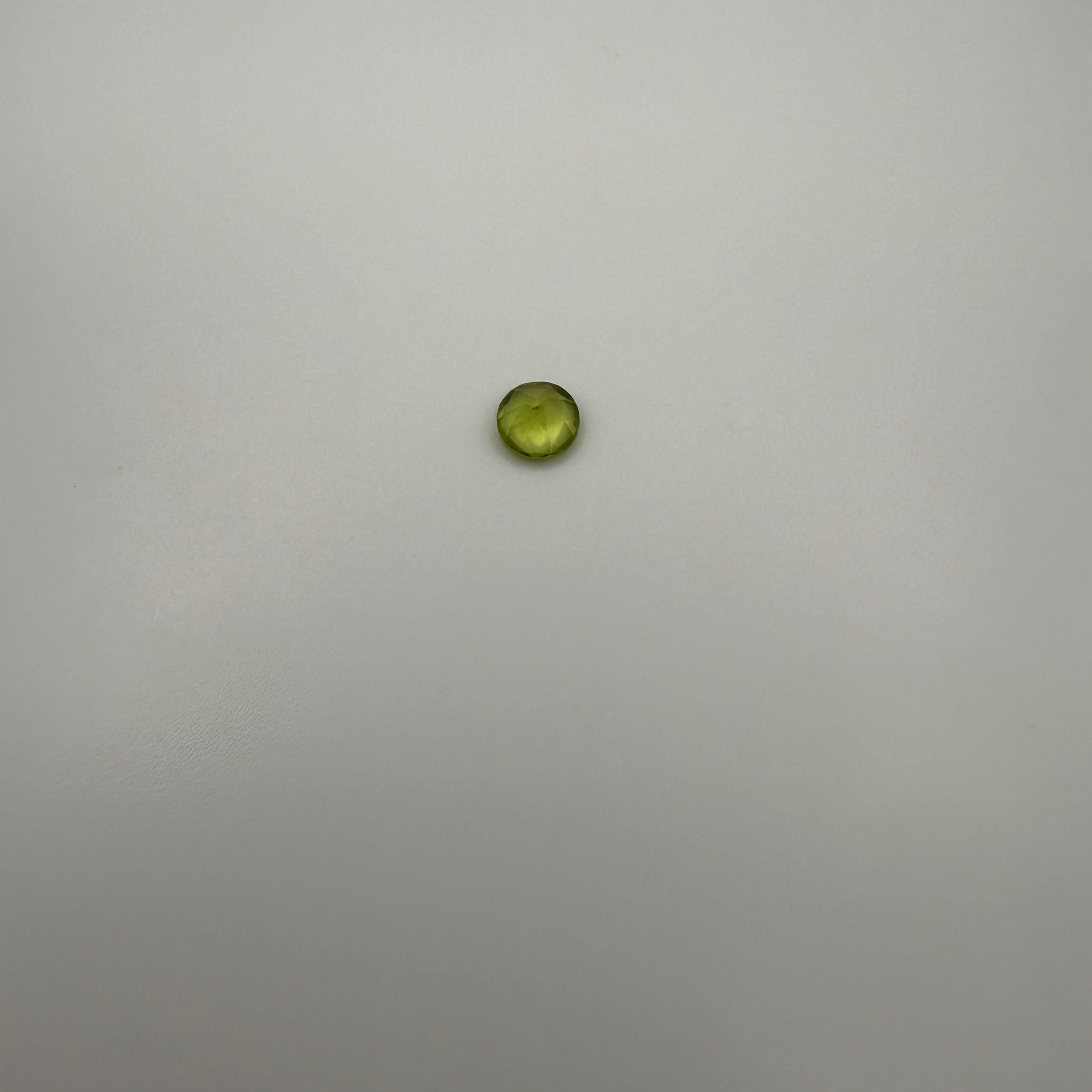 Round faceted 0.45ct yellow-green peridot gemstone on a light background