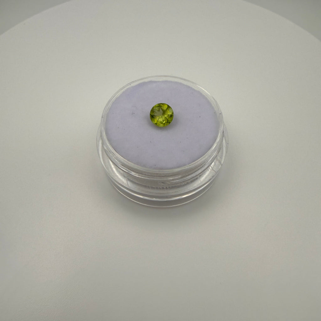 Round faceted 0.45ct yellow-green peridot gemstone displayed in a clear holder on soft surface