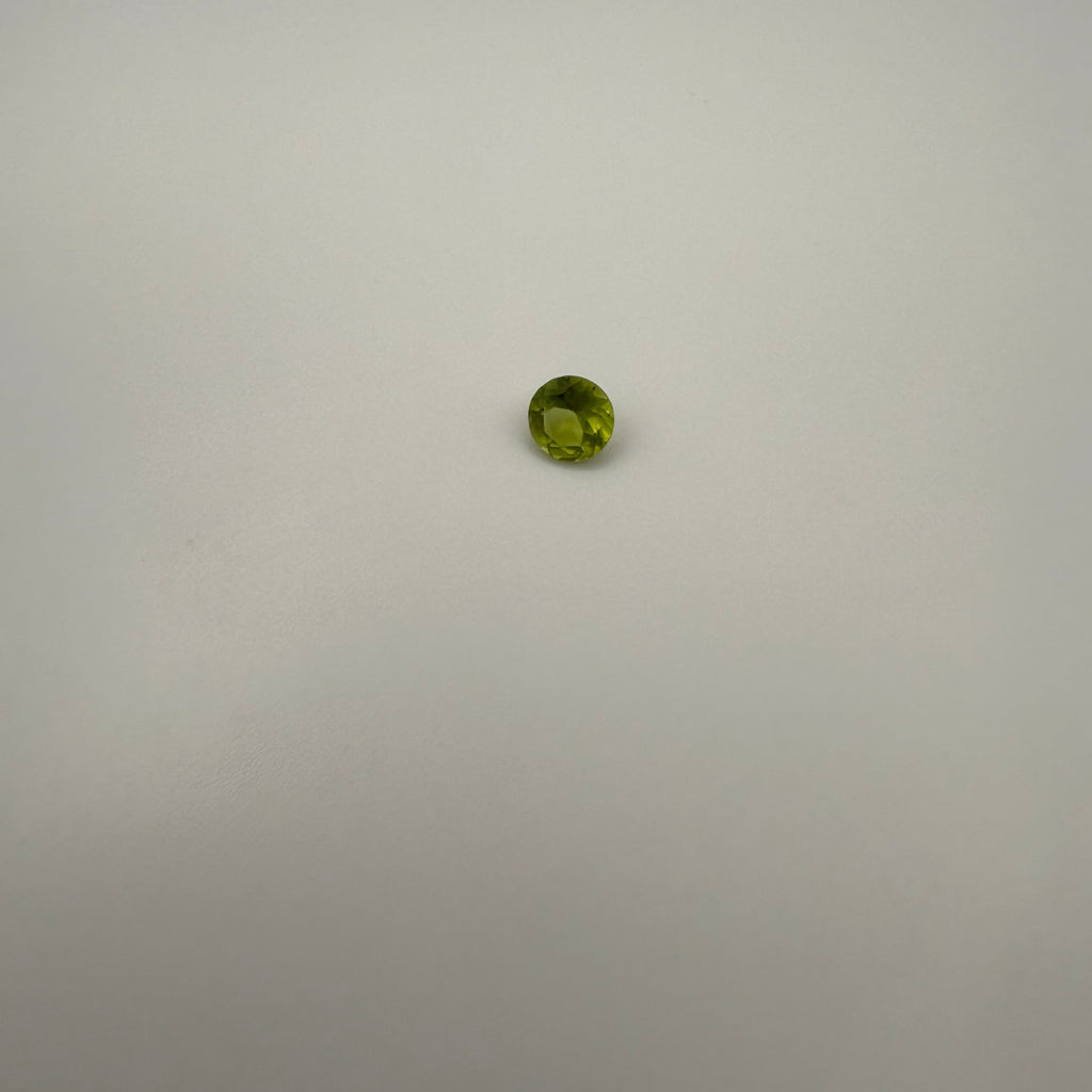 0.45ct round faceted yellow-green peridot gemstone on a smooth light surface