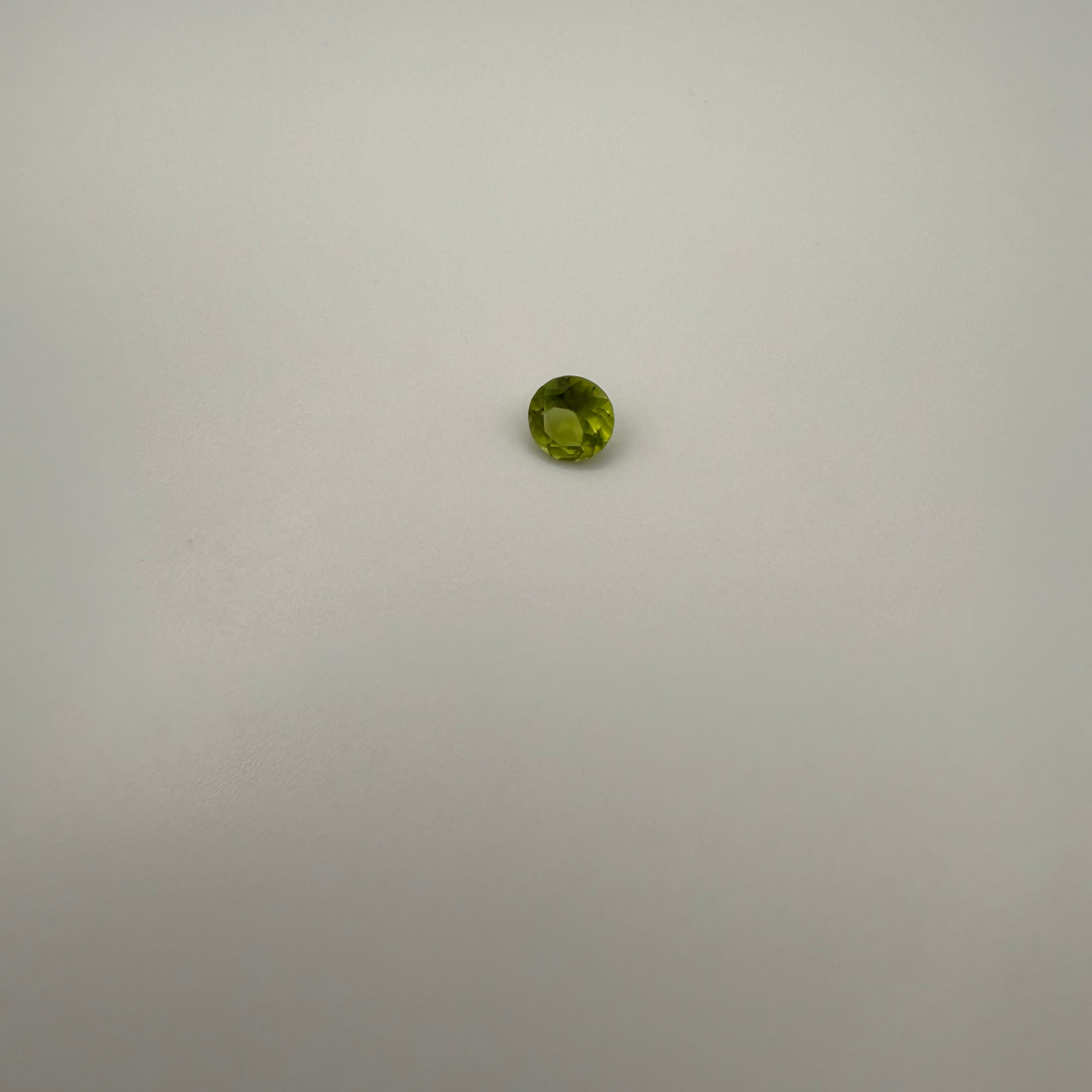 0.45ct round faceted yellow-green peridot gemstone on a smooth light surface