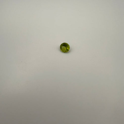 0.45ct round faceted yellow-green peridot gemstone on a smooth light surface