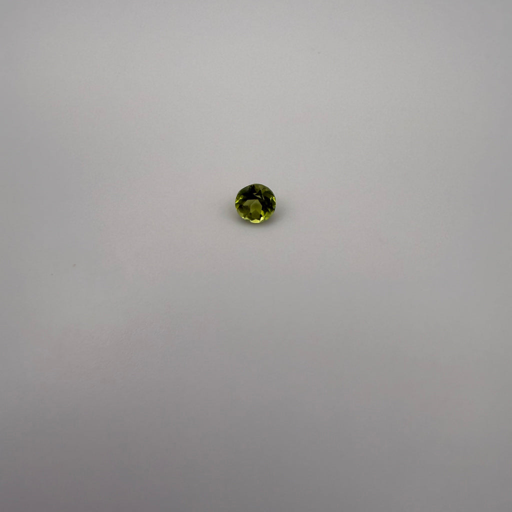 macro view of 0.5ct round faceted yellow-green peridot gemstone on neutral background