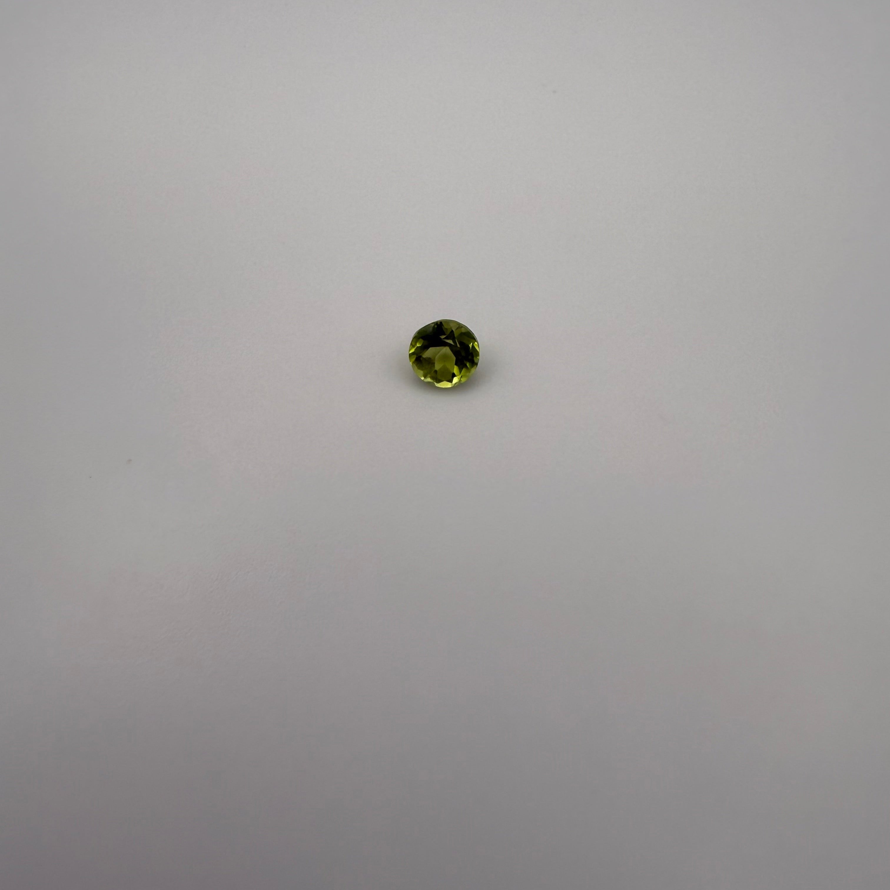 macro view of 0.5ct round faceted yellow-green peridot gemstone on neutral background