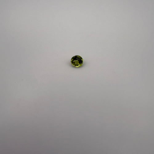 macro view of 0.5ct round faceted yellow-green peridot gemstone on neutral background